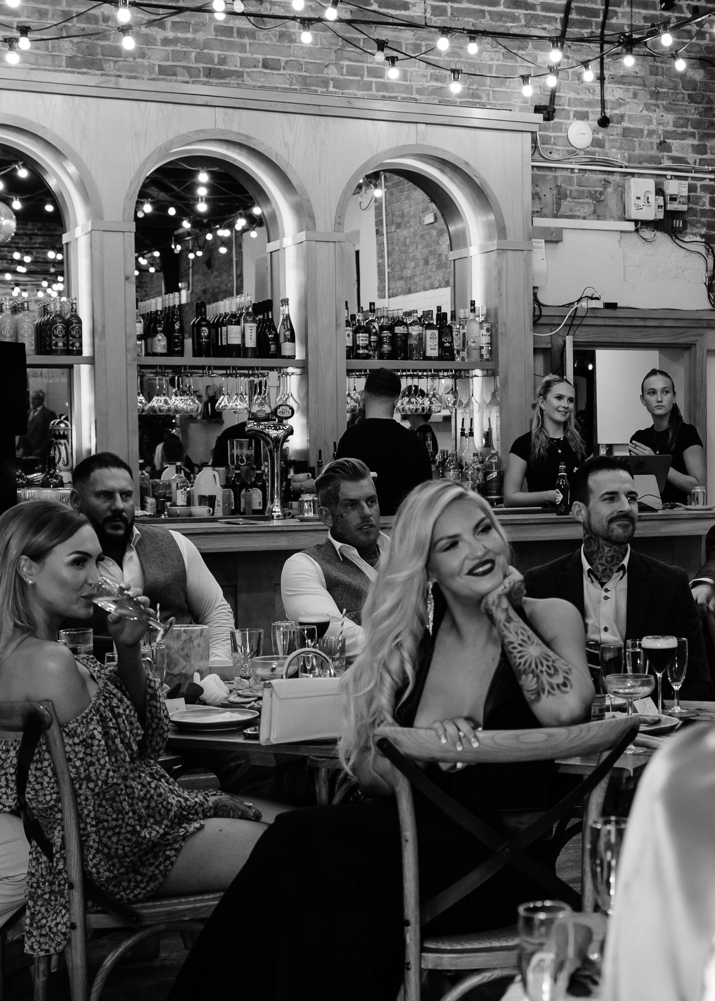 Diners enjoying a lively evening at a restaurant with string lights and brick walls creating an intimate atmosphere.