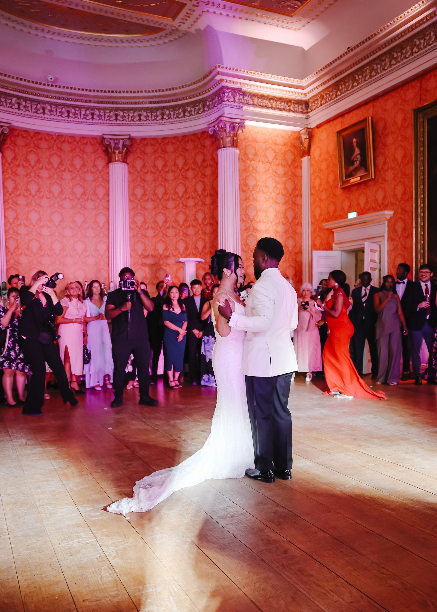 Couples dancing together at an elegant wedding reception in a grand ballroom with ornate pink walls and moldings.