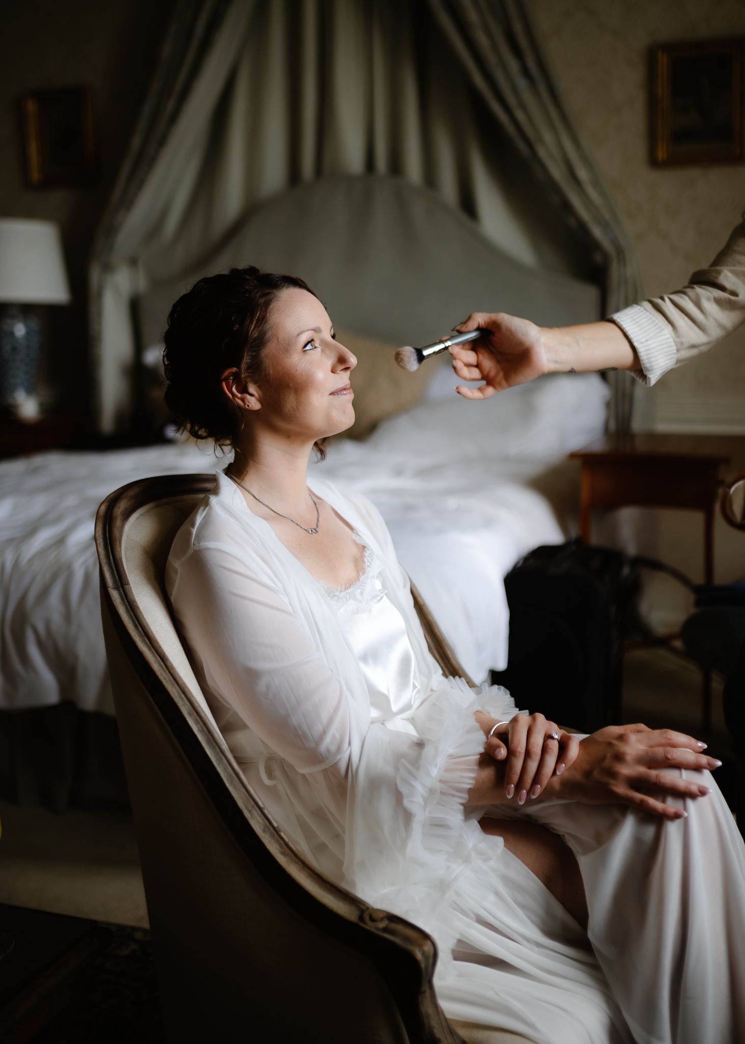 A person in a white blouse sits in a chair while someone's hand reaches toward them in a dimly lit room.