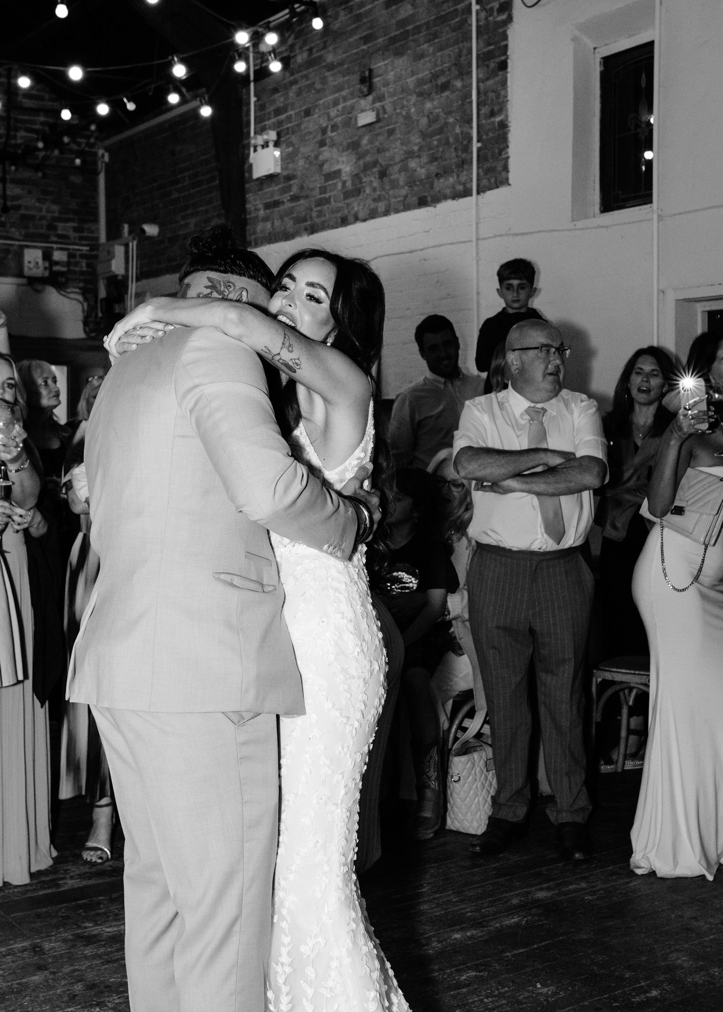 Wedding guests dance and celebrate on a dimly lit dance floor decorated with string lights overhead.