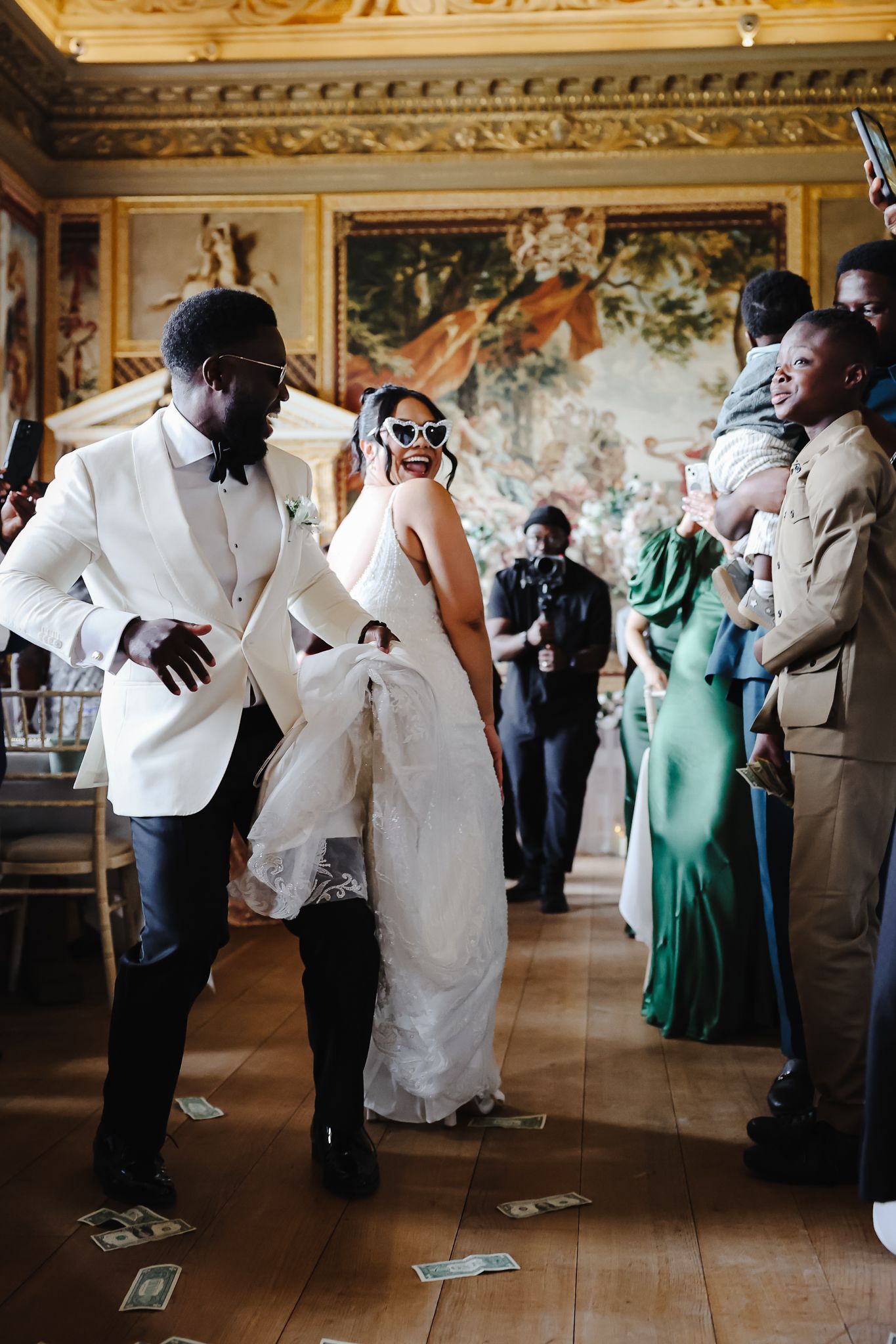 Wedding party dancing and celebrating in an ornate ballroom with gilded details.