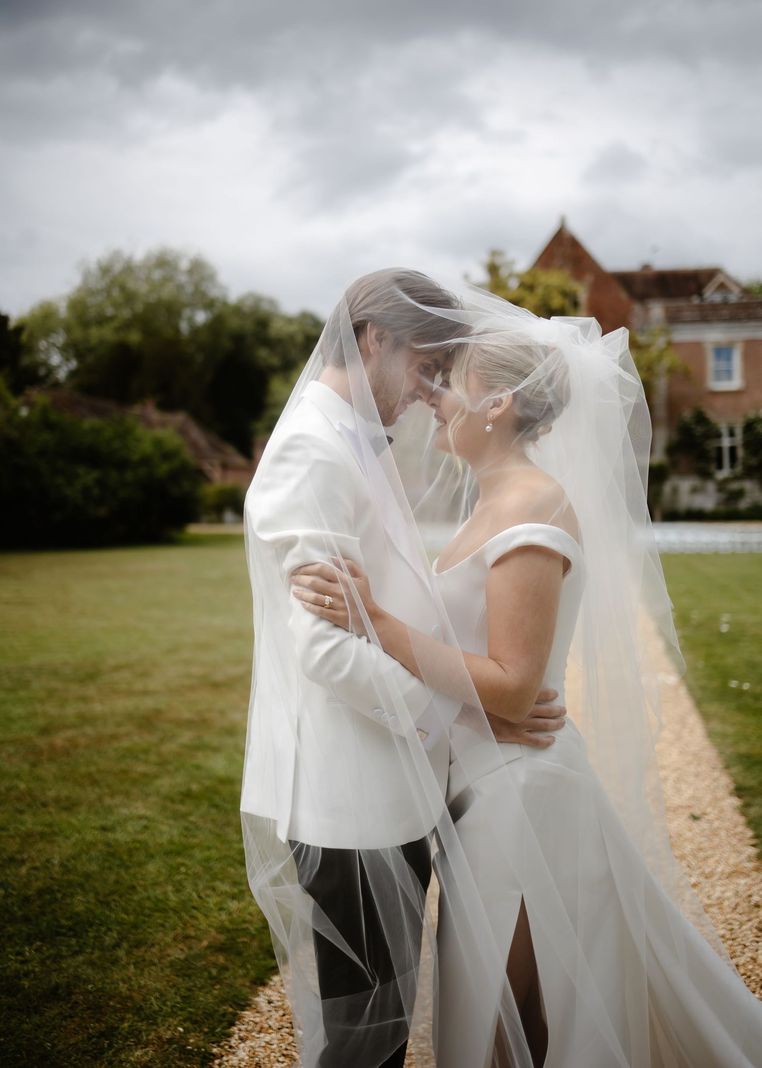 Bride and groom share a romantic kiss under a flowing wedding veil outdoors at an English country estate.