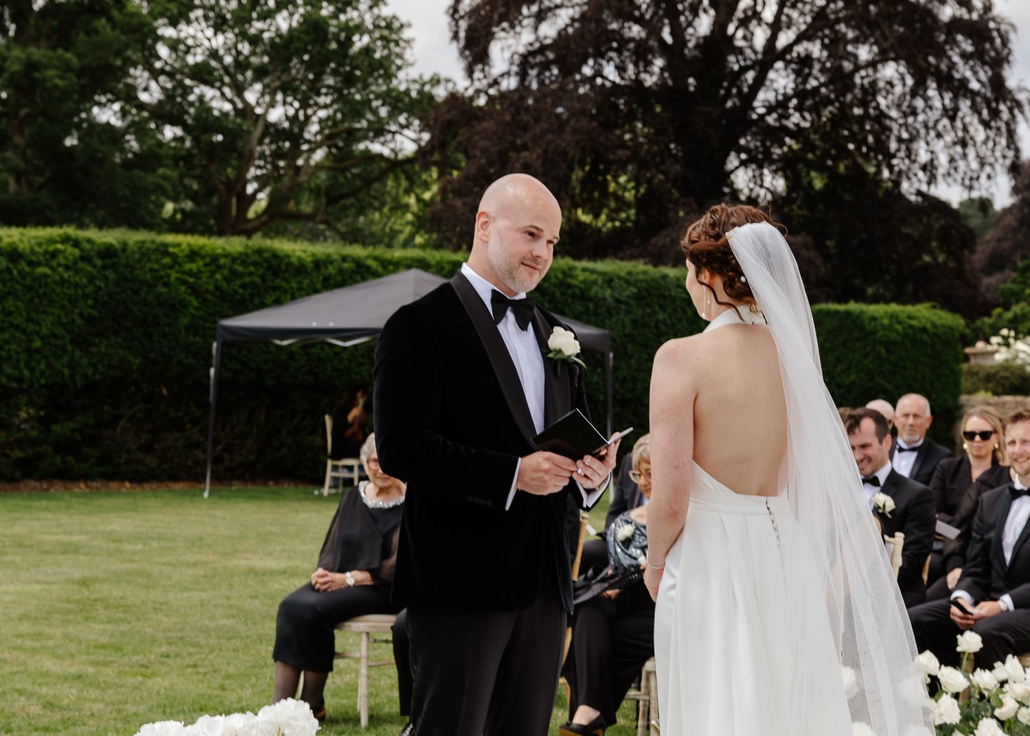 Wedding party stands together during outdoor ceremony in elegant formal attire and floral arrangements.