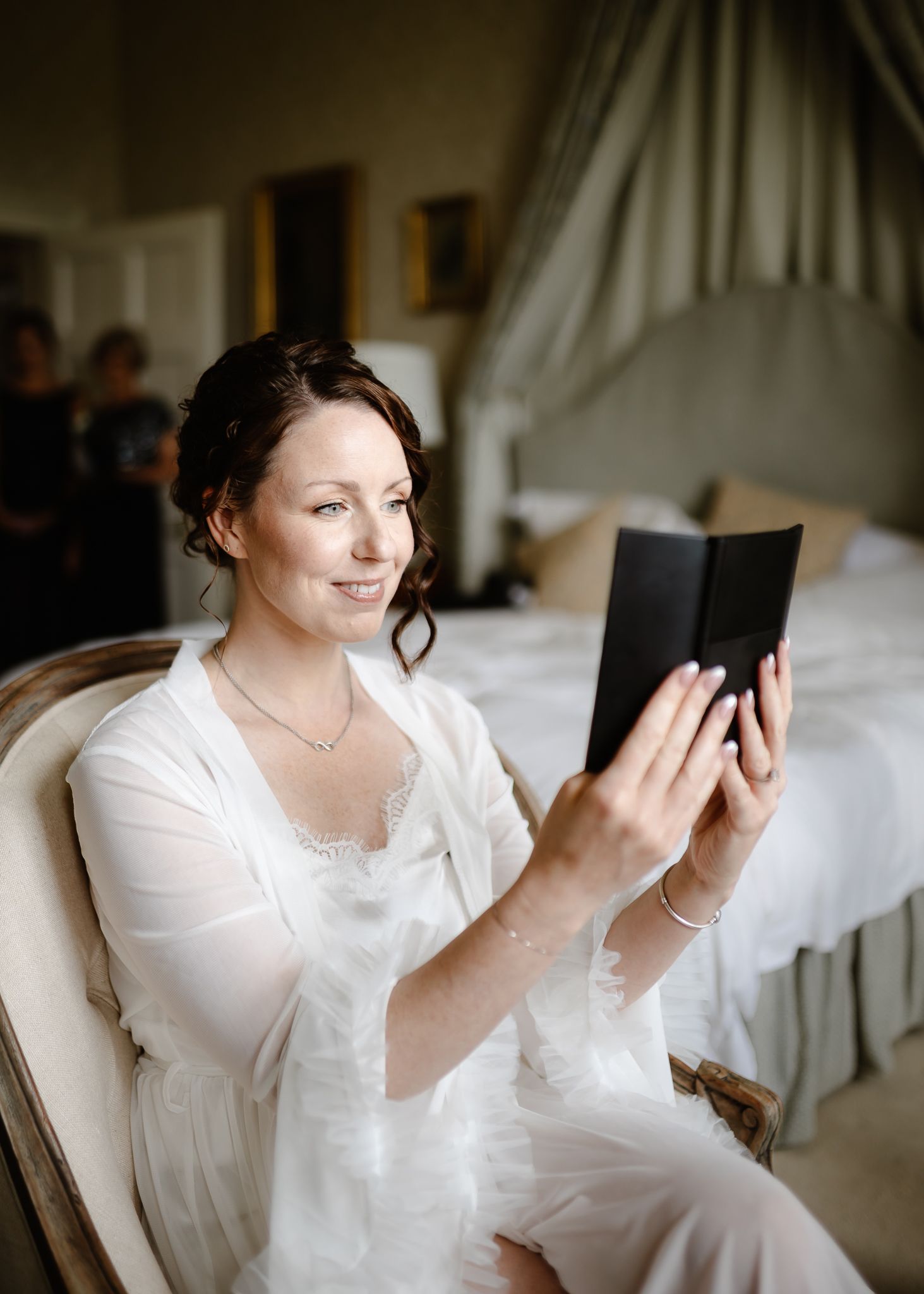 A person in a white robe sits on a sofa while looking at a mobile phone in a sunlit room.