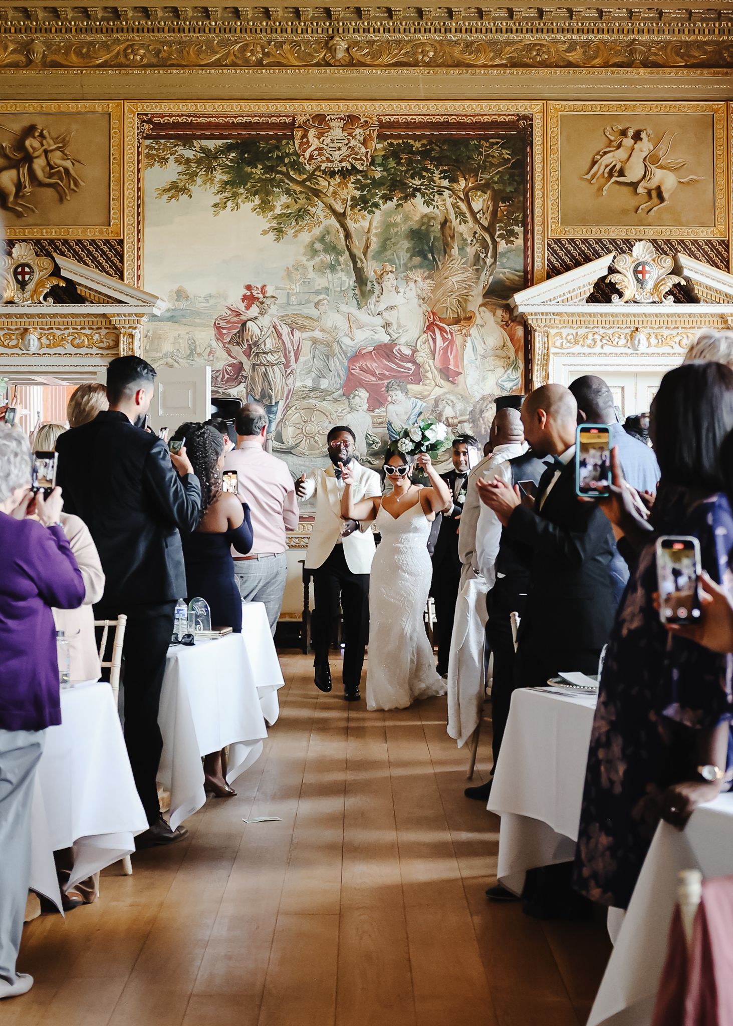 Wedding reception in an elegant ballroom with white-clothed tables and classical painted walls and ceilings.