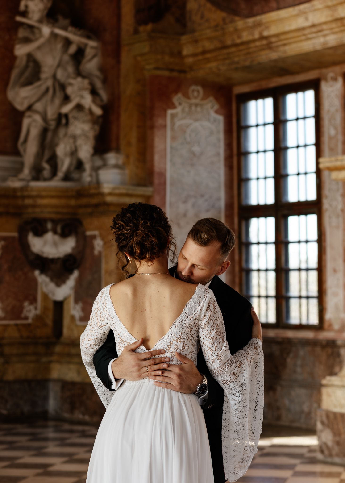 A tender wedding moment captured in a historic ballroom with decorative wall sculptures.