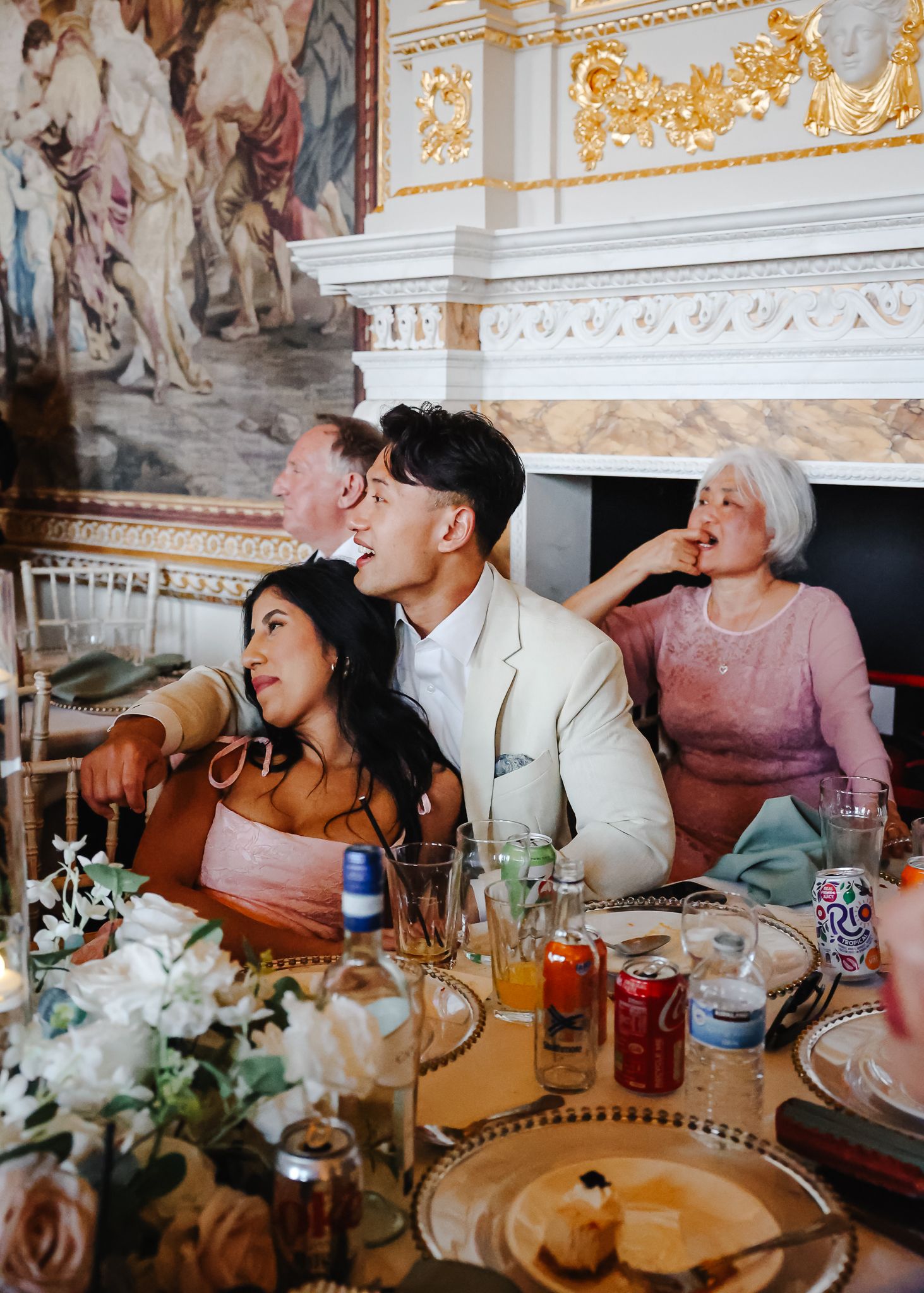 Wedding guests enjoy dinner and drinks in opulent room with gilded details and classical murals.