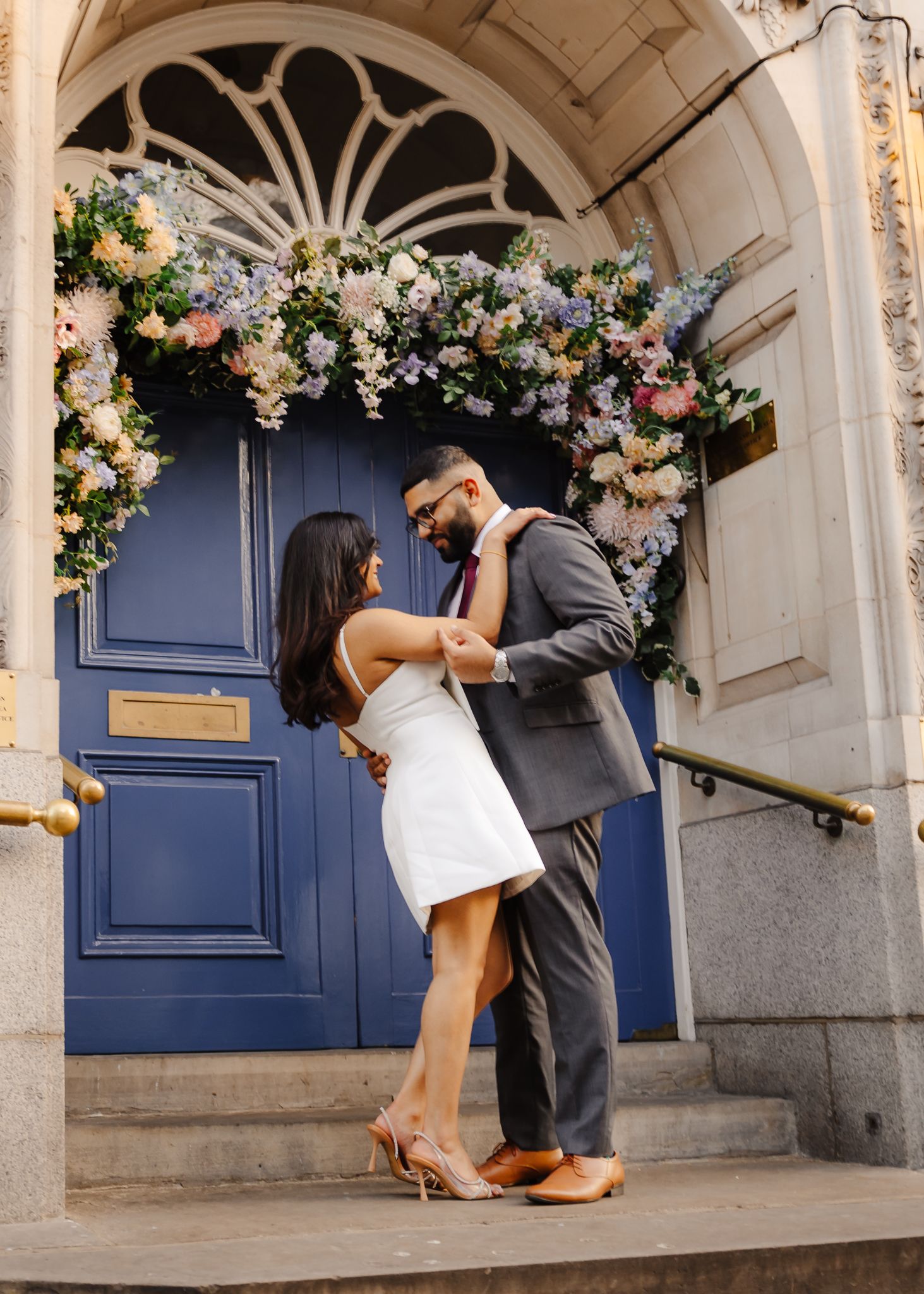 Couple dancing romantically in front of a blue door adorned with a floral arch in London.