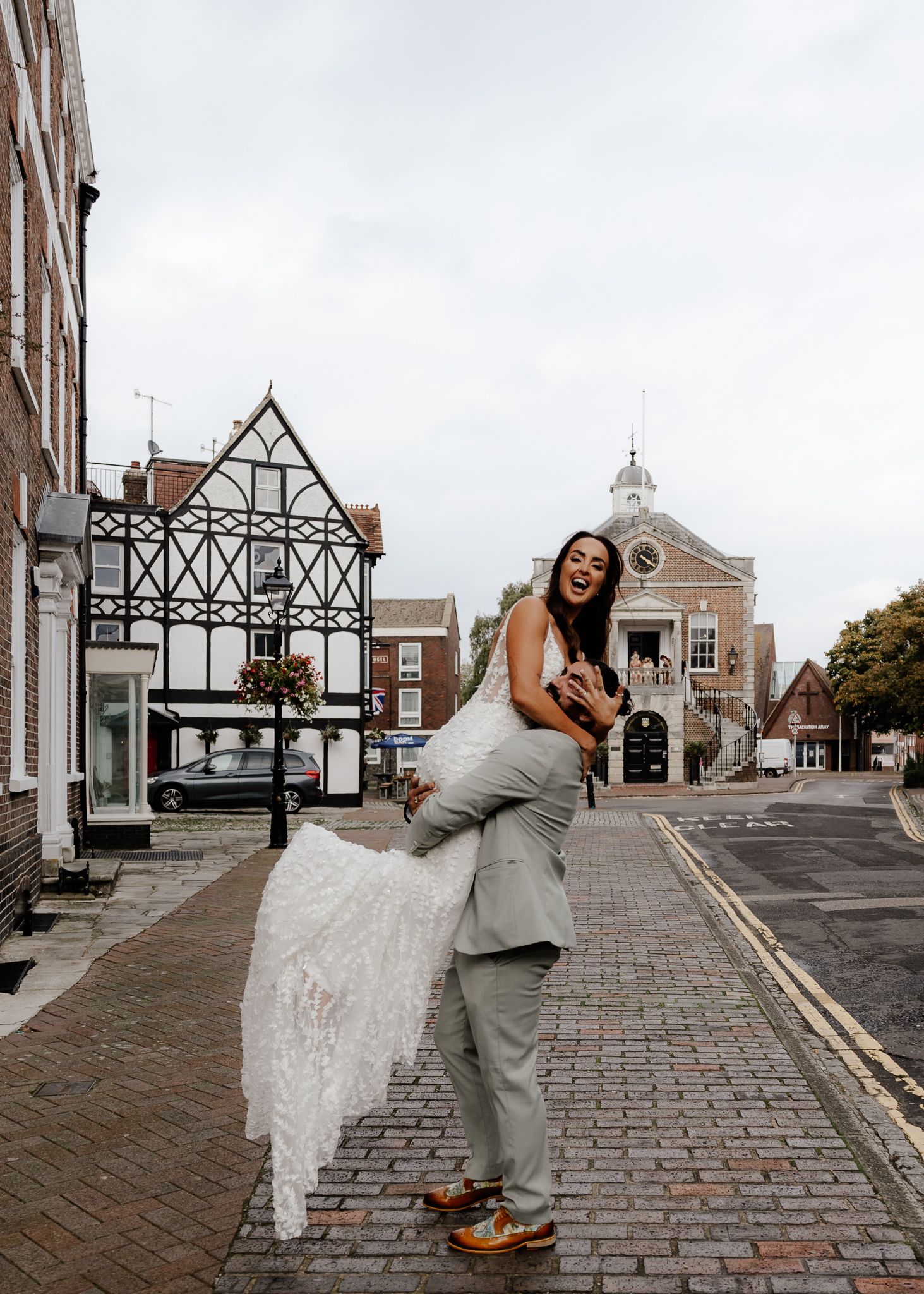 A joyful couple dances on cobblestone streets in front of a historic Tudor-style building.
