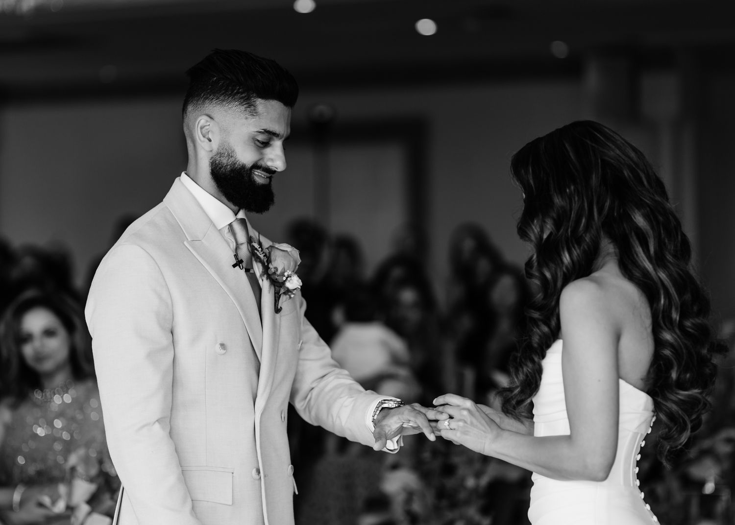 A black and white photo of a wedding ceremony as a couple exchanges rings during an intimate indoor moment.
