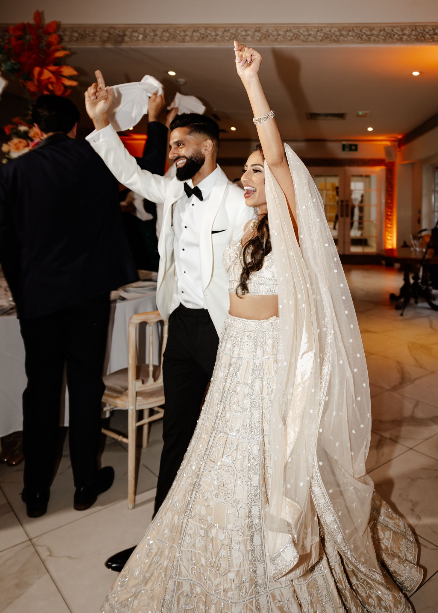 A couple in wedding attire dances together on a white marble floor during their reception celebration.