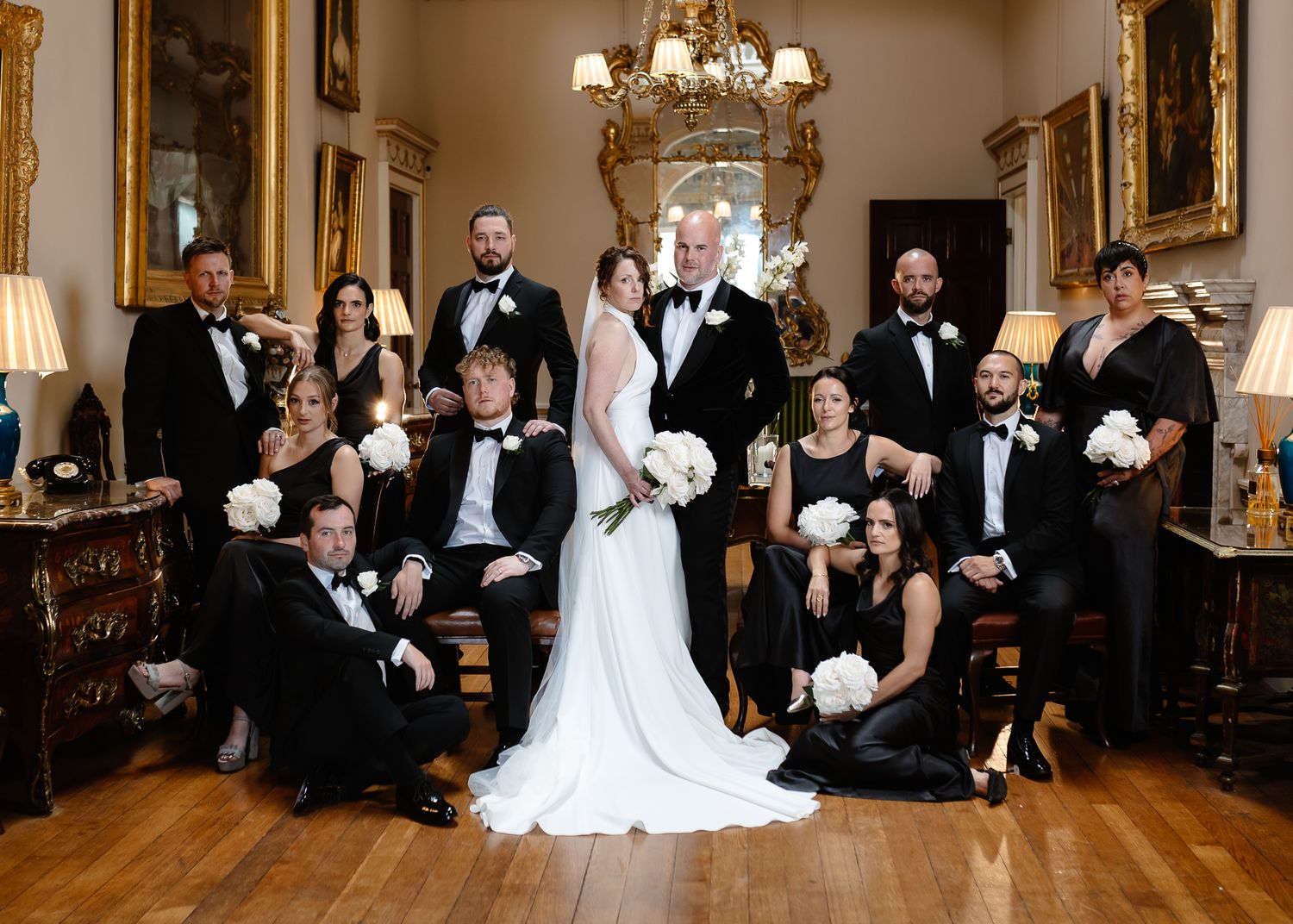 Wedding party poses together in an elegant room with chandeliers and ornate gold mirrors.