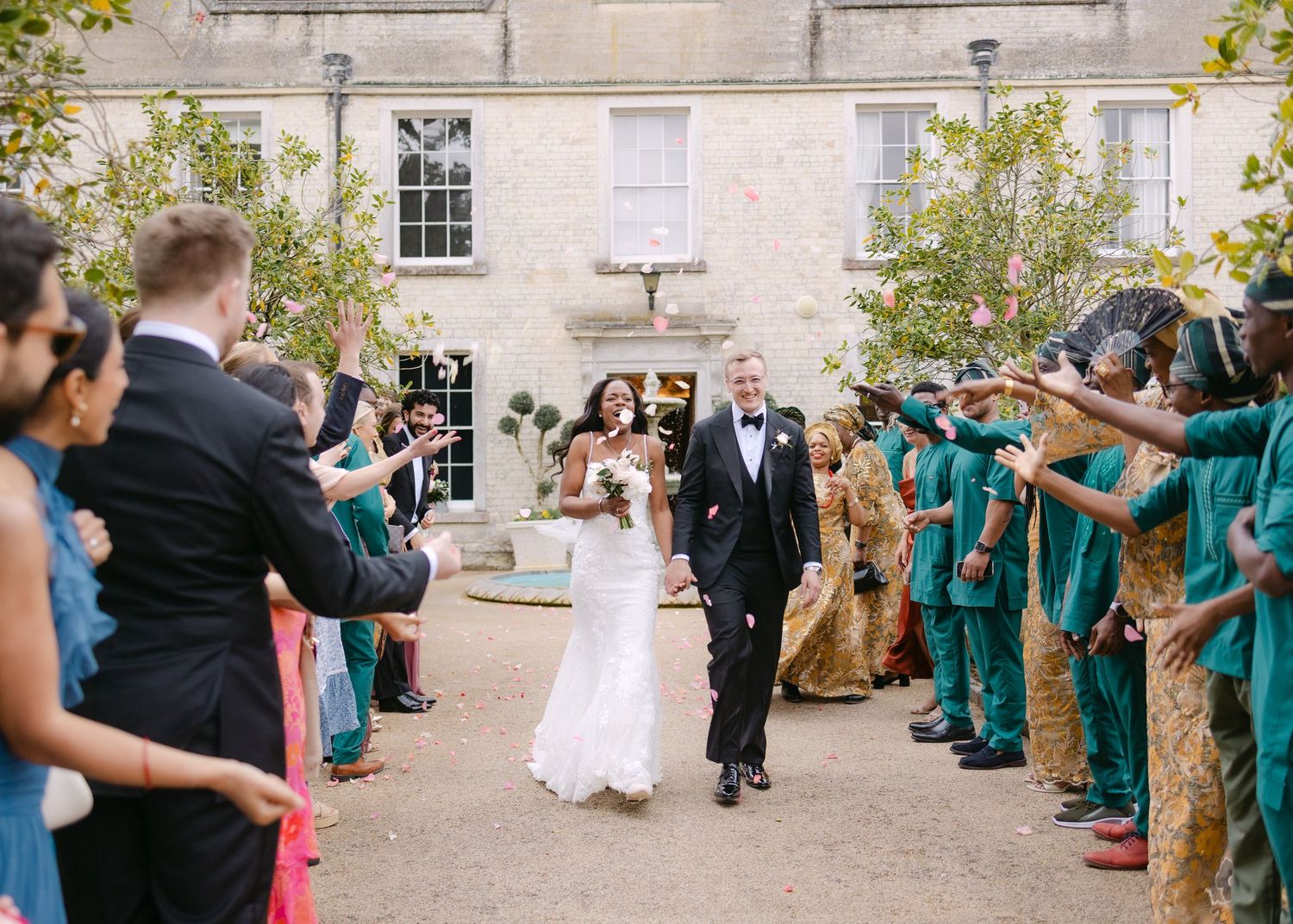 Bride and groom walk through cheering guests in a joyful outdoor wedding exit at an elegant stone manor.
