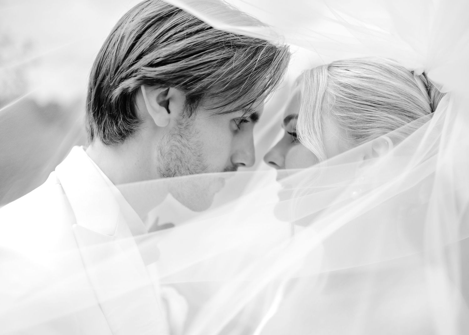 Black and white wedding photo of bride and groom sharing an intimate moment under a flowing veil.