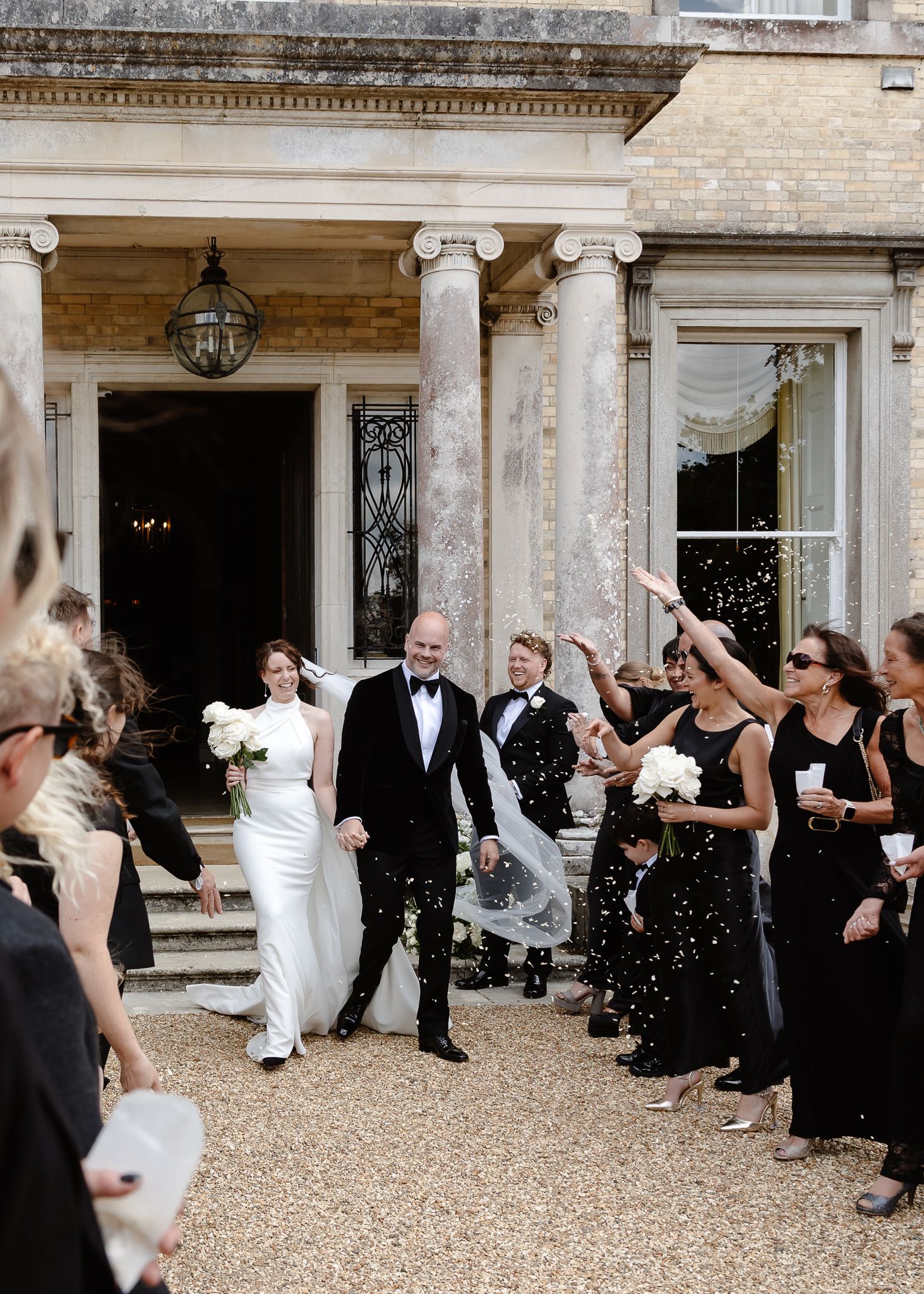 Wedding celebration outside historic building with guests throwing confetti.