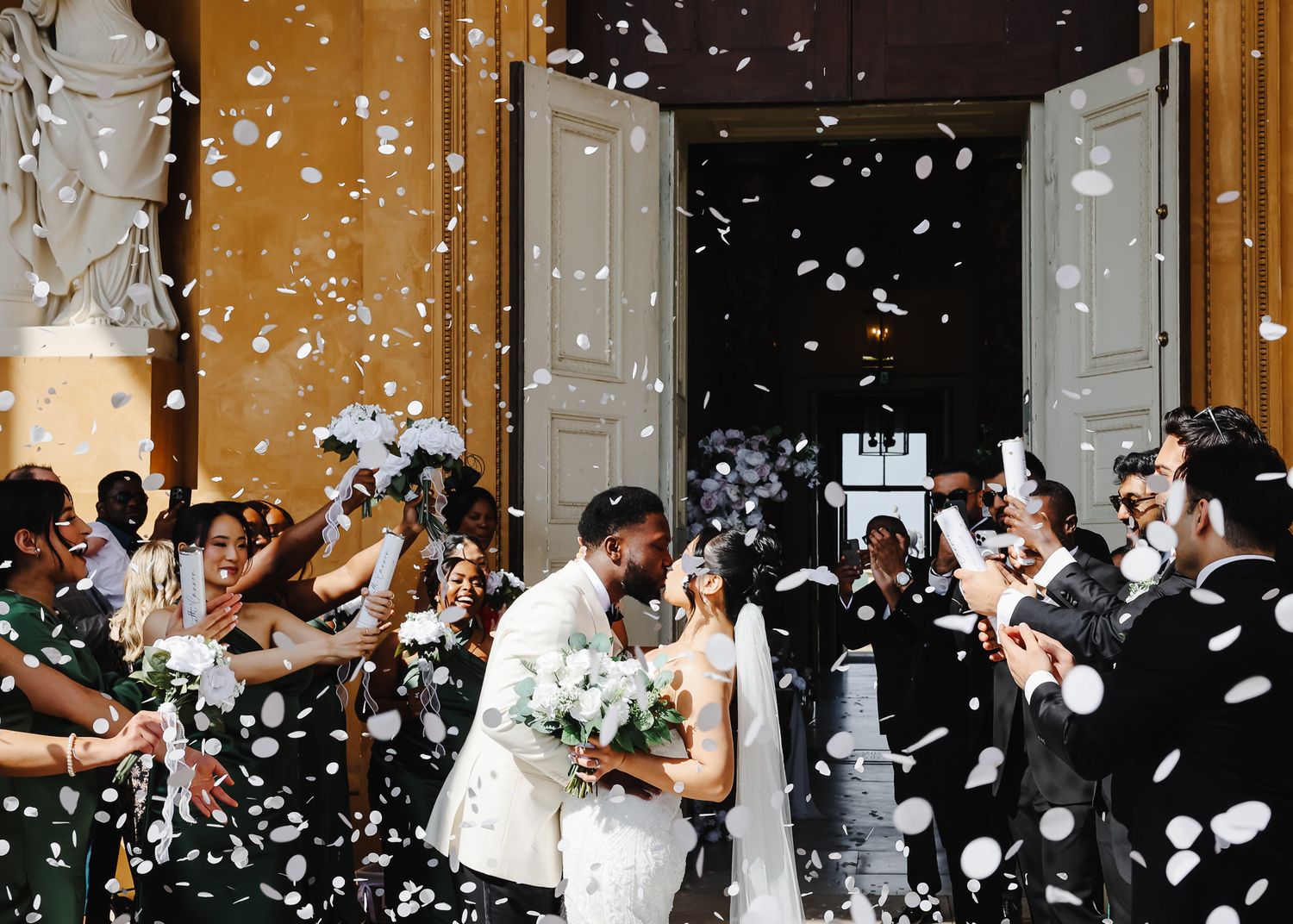 Newlyweds exit their wedding ceremony under a shower of white confetti while guests celebrate their joyful moment.