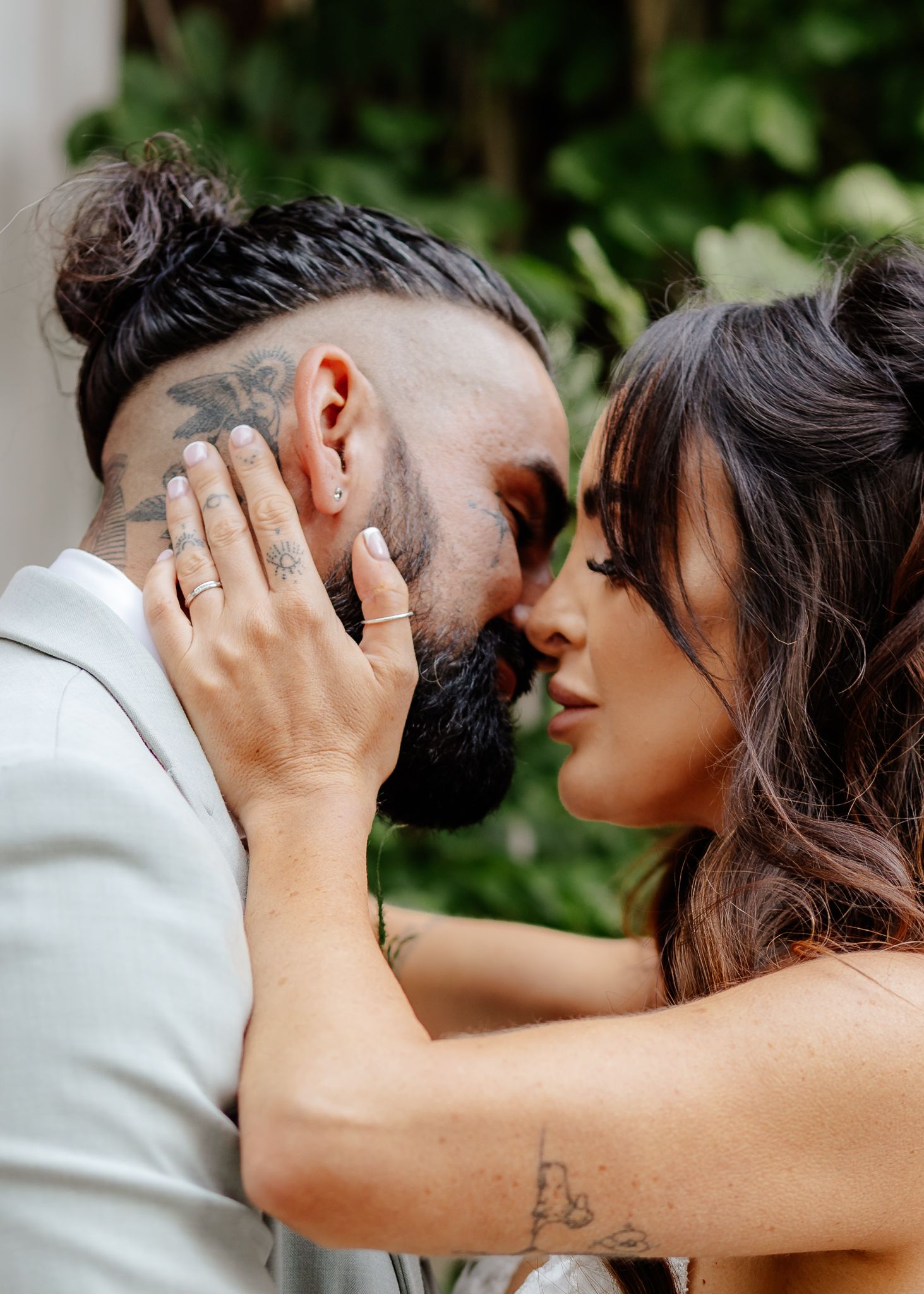 A romantic couple shares an intimate moment in a garden setting with hands caressing faces.
