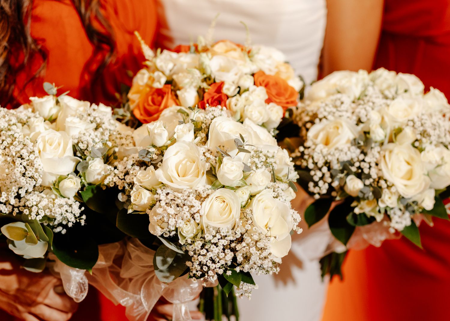 A row of elegant white and cream wedding bouquets with roses and baby's breath against a red background.
