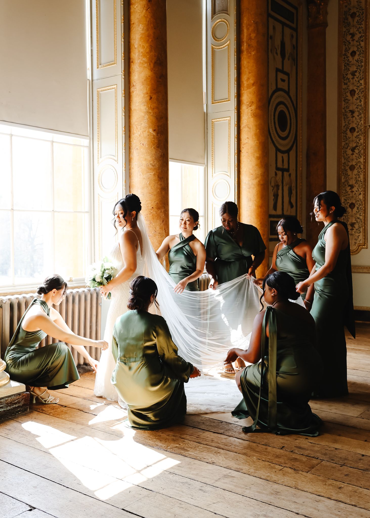People sitting in a row by large windows in an elegant room with ornate columns and sunlight streaming in.