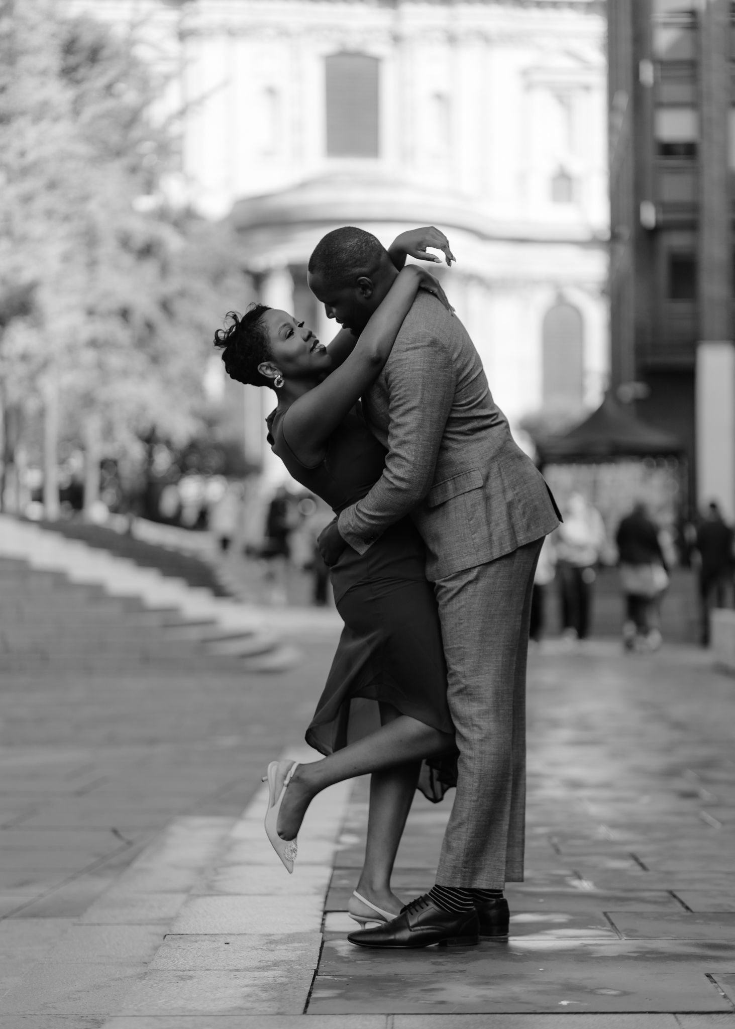 A romantic couple in vintage clothing dips and embraces in a classic dance pose on a city sidewalk.