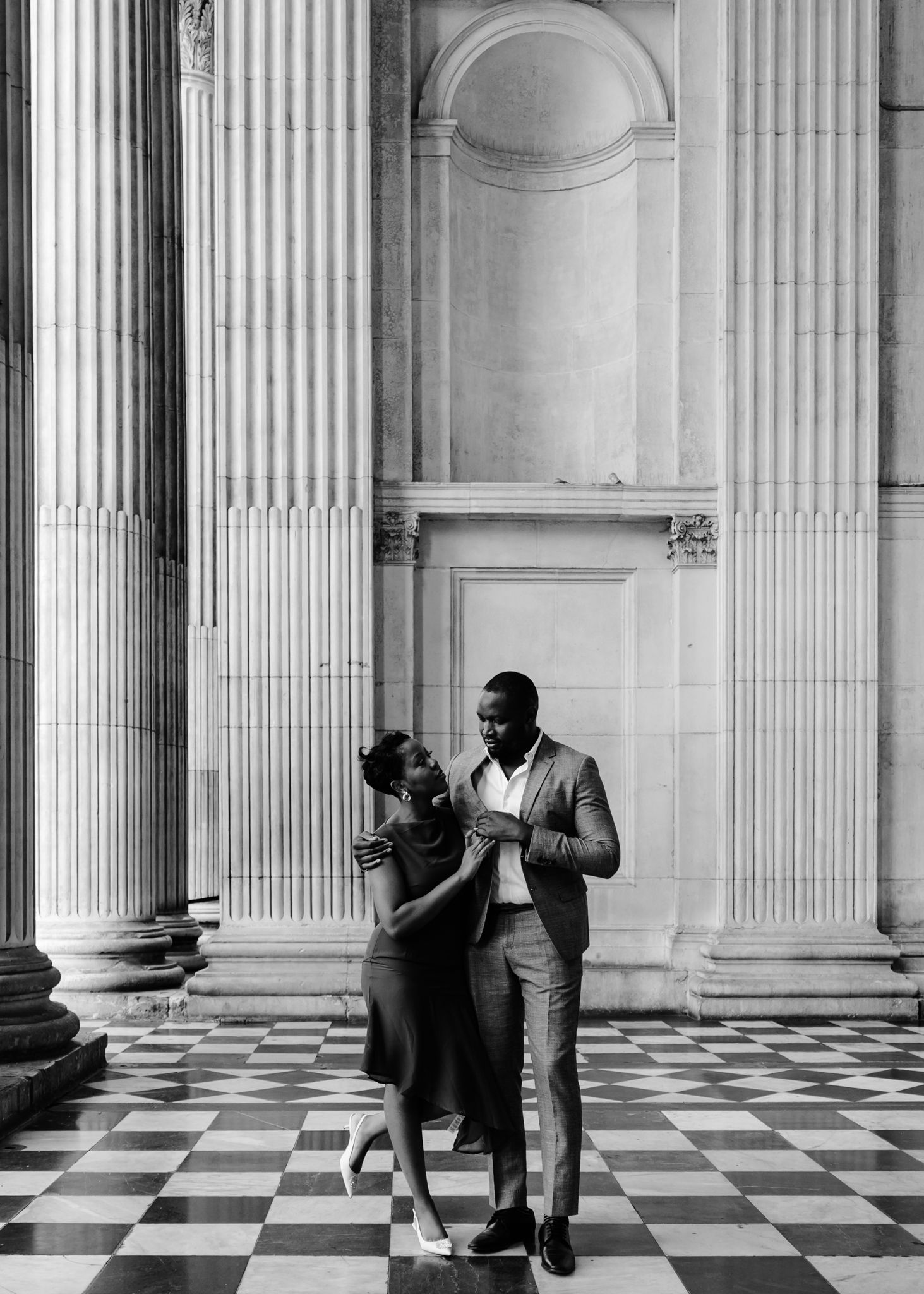 People in formal attire walk through a grand interior space with checkered floors and classical columns at St Paul's Cathedral.