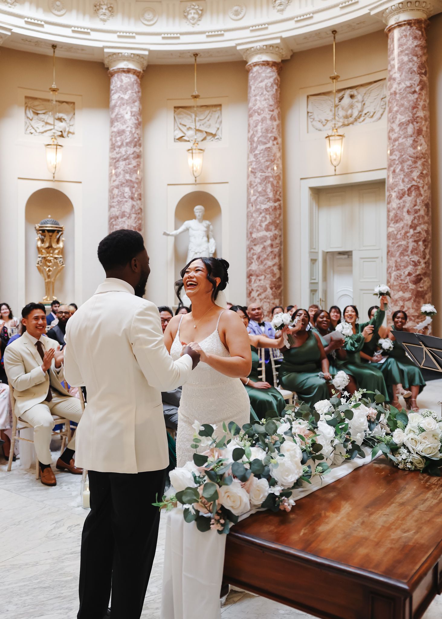 A joyful wedding celebration takes place in an elegant marble rotunda with ornate columns and classical architectural details.