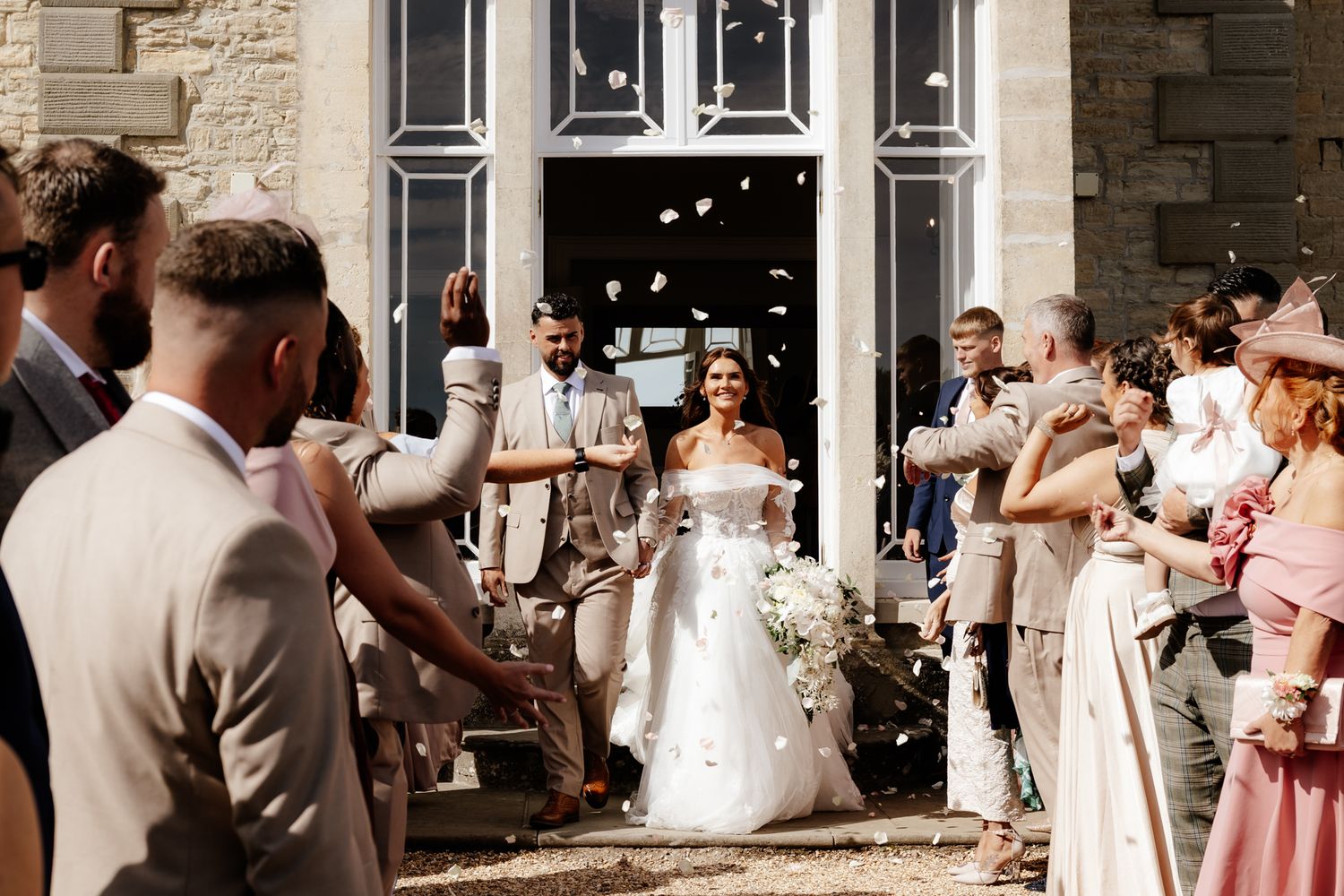 Wedding party celebrates with confetti and bubbles outside an elegant stone venue.