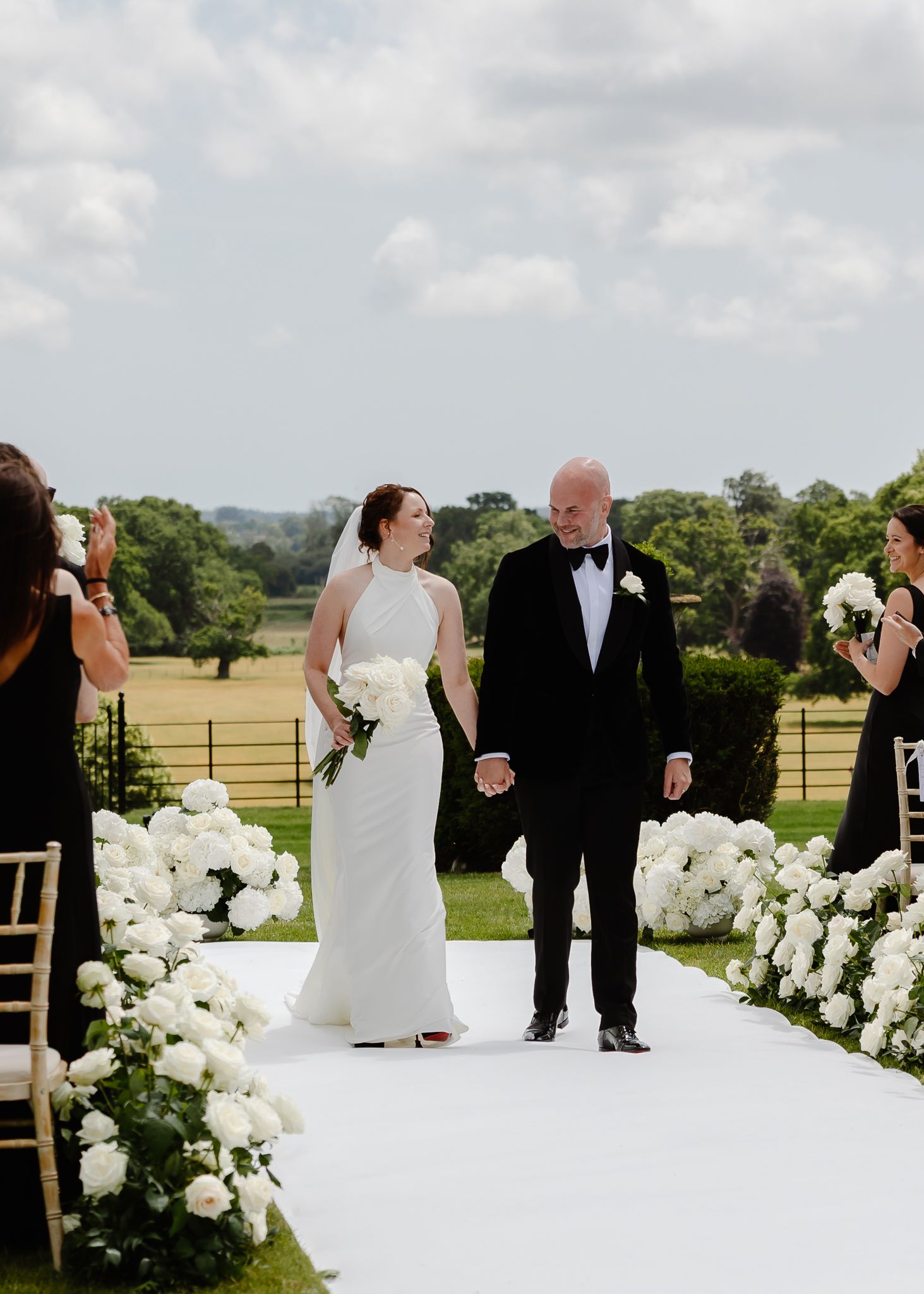 Wedding ceremony setup outdoors with white floral arrangements and aisle decorations on a sunny day.