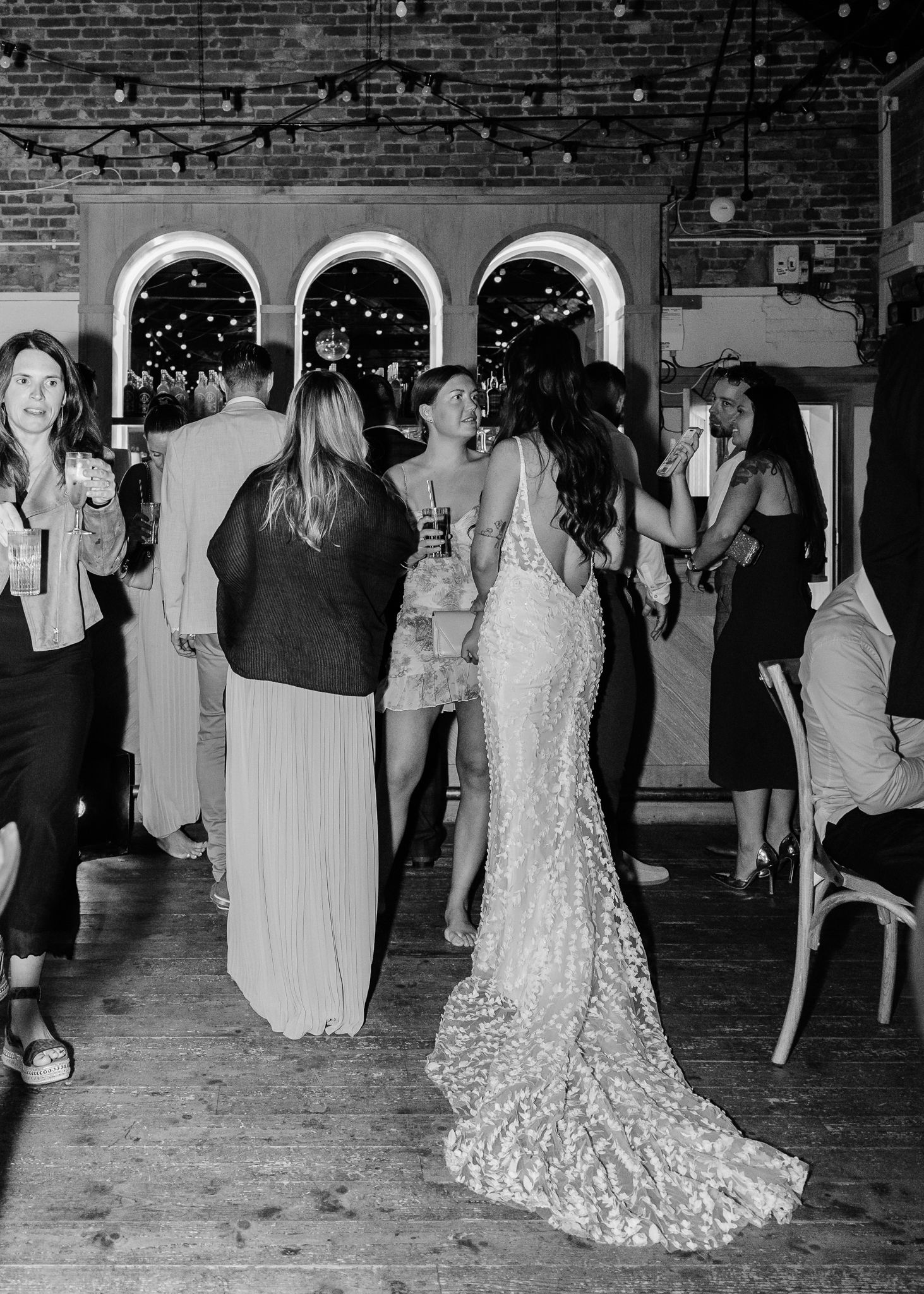 A panoramic view of a wedding reception showing guests mingling and dancing in a rustic brick-walled venue.