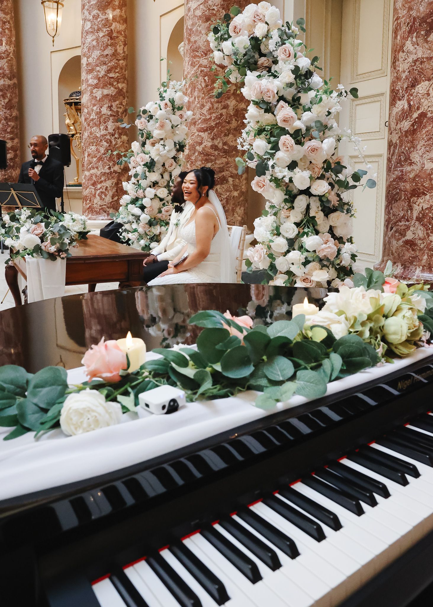A piano keyboard adorned with elegant white floral arrangements and eucalyptus leaves creates a romantic wedding setting.