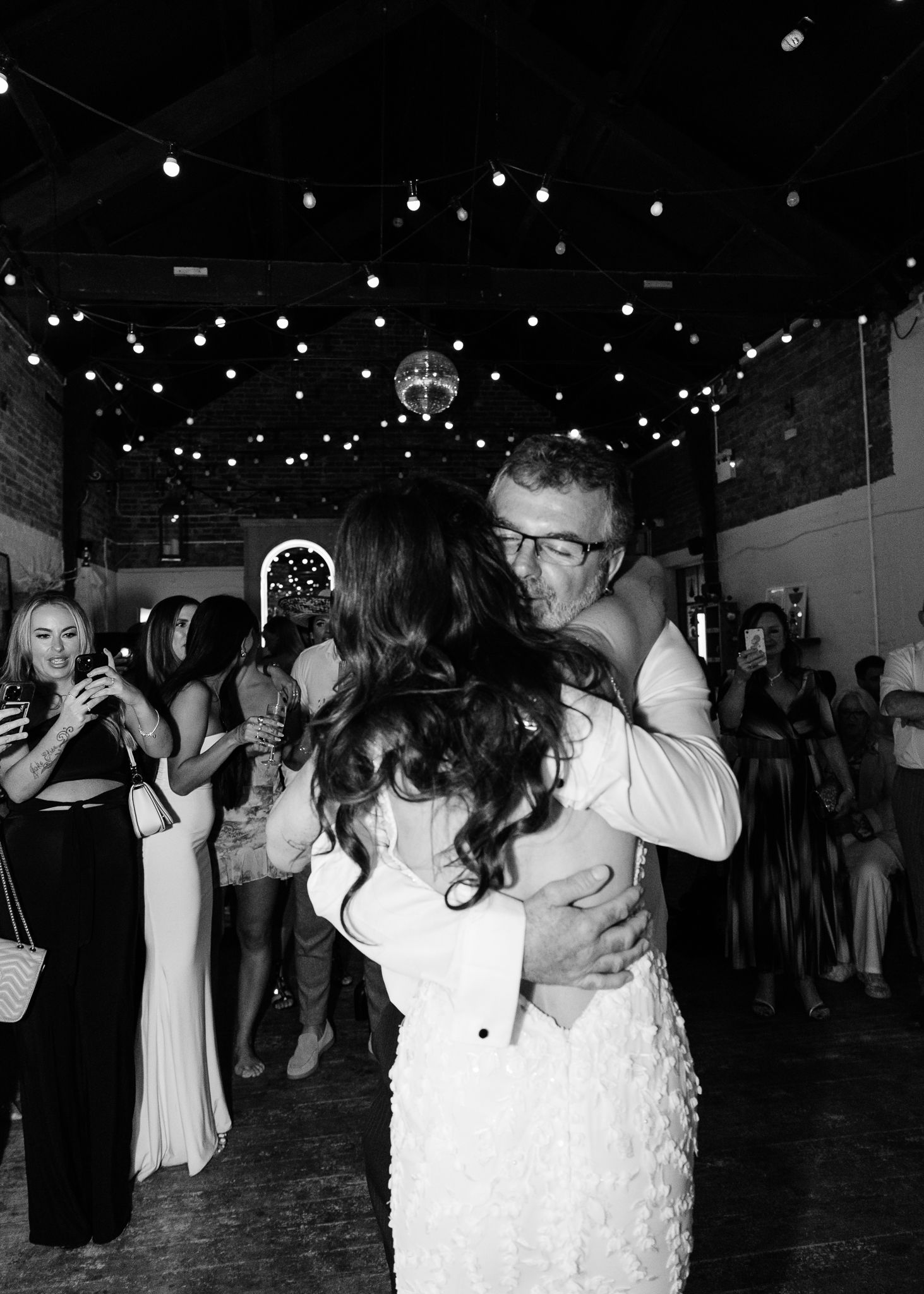 Couples dance together under twinkling string lights at an outdoor evening celebration.