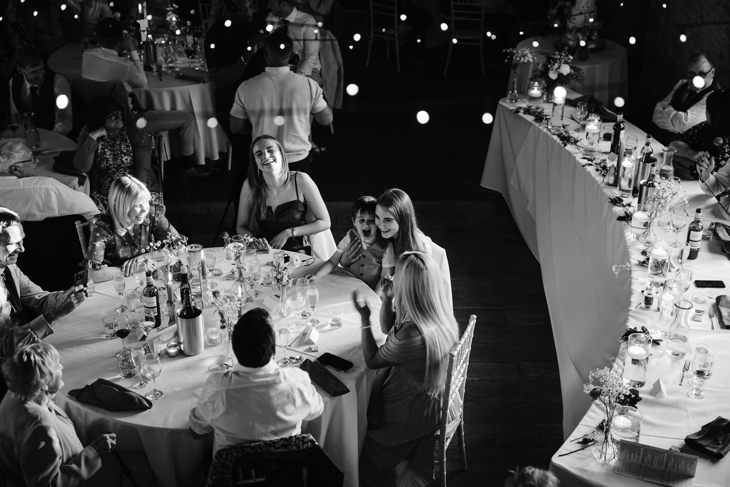 Wedding guests dance under twinkling lights at an evening reception celebration.