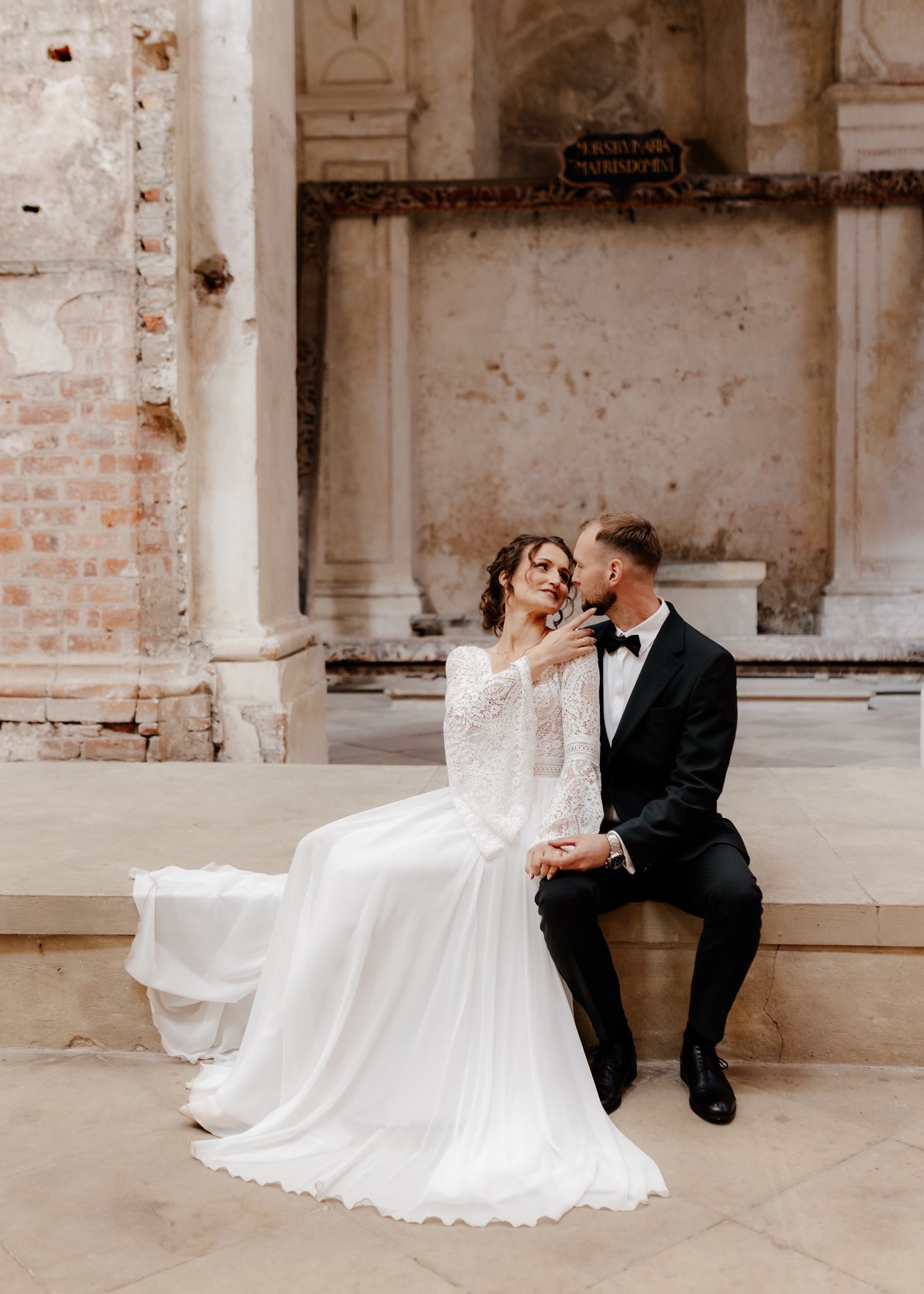 Wedding couple poses in a rustic venue with exposed brick walls and natural lighting.
