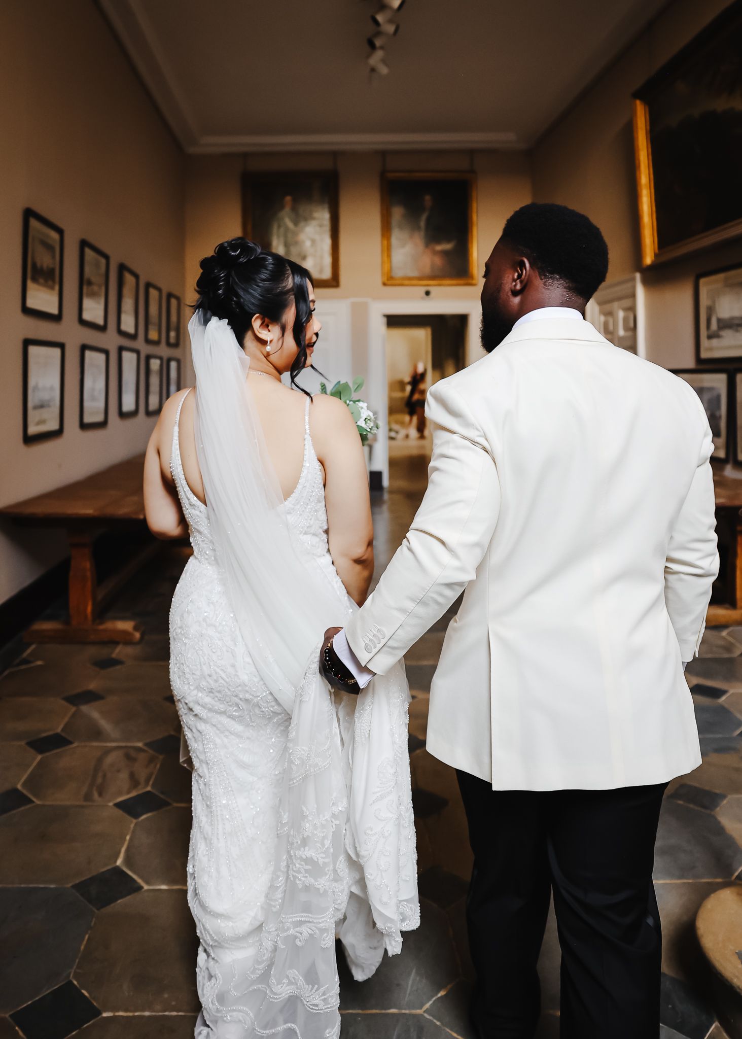 Back view of wedding party walking through indoor venue in white and black formal attire.