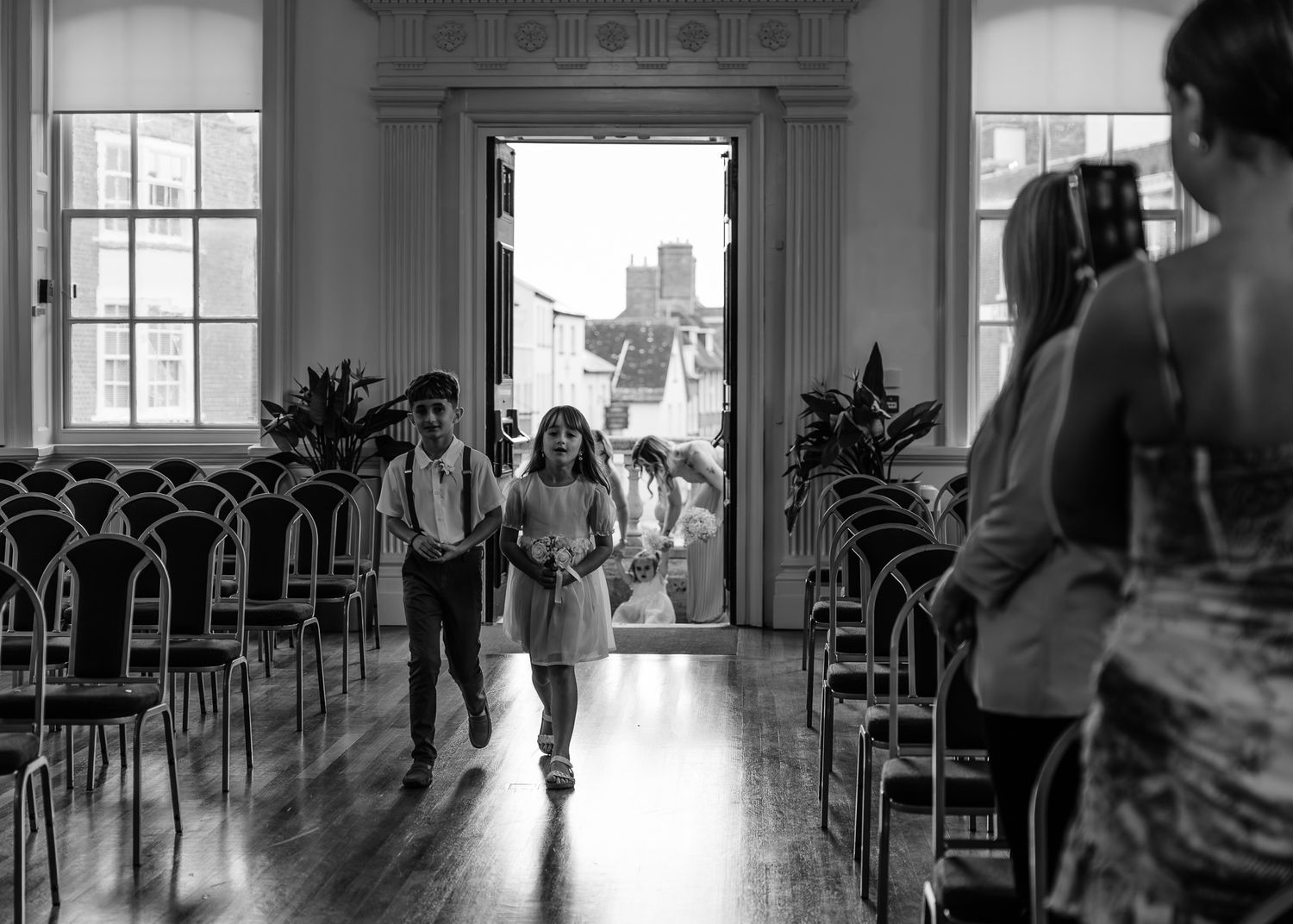 A black and white panoramic view of a dance studio with windows and dancers practicing in silhouette.