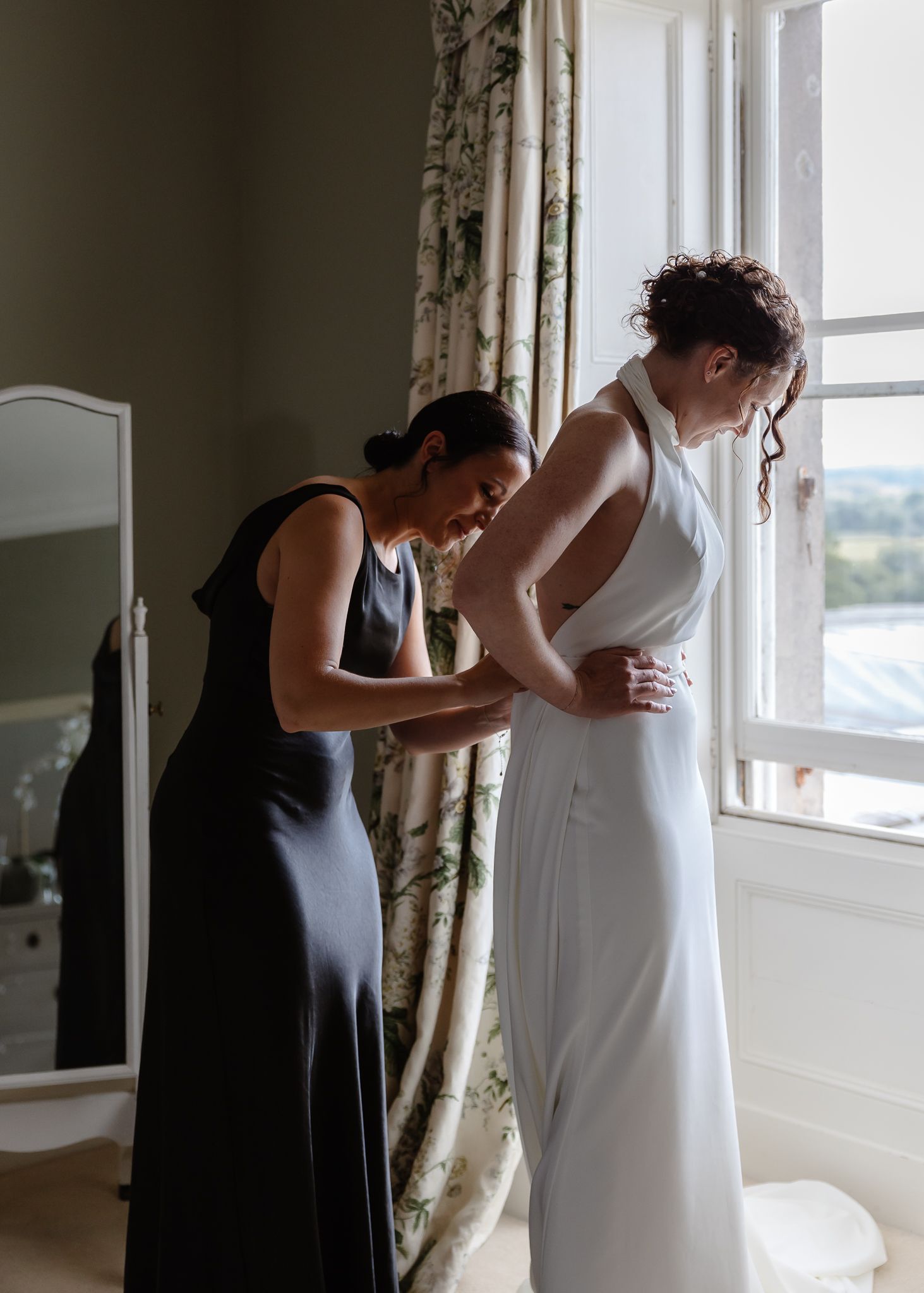 Multiple sequential shots show someone in white adjusting their footwear by a bright window with decorative drapes.