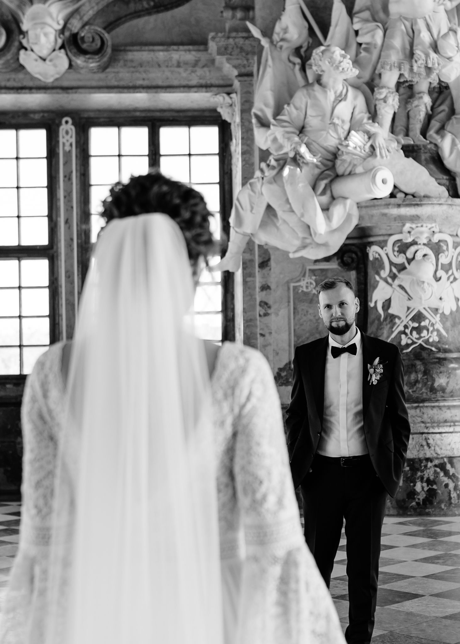 Black and white wedding photo showing a couple in a grand baroque interior with ornate architectural details and sculptures.