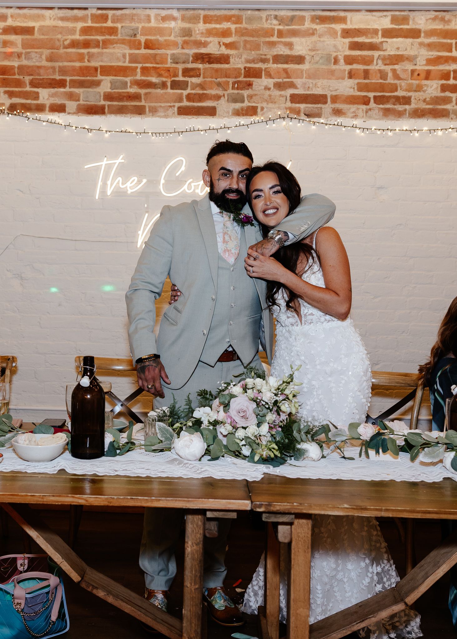Couple shares a candid moment while sitting at a rustic wooden table during their wedding reception.