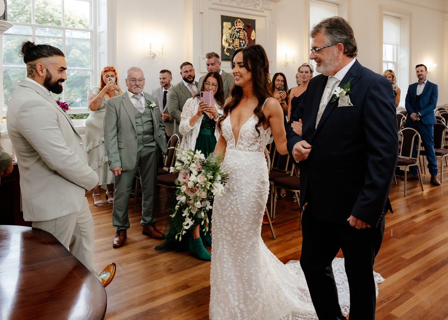 Wedding ceremony in a bright indoor venue with polished hardwood floors and guests watching the joyful celebration.