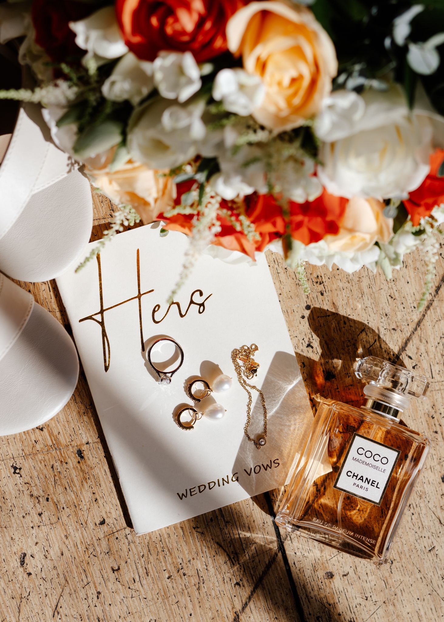 Elegant wedding invitation details with Chanel perfume bottle and coral flowers on rustic wooden background.