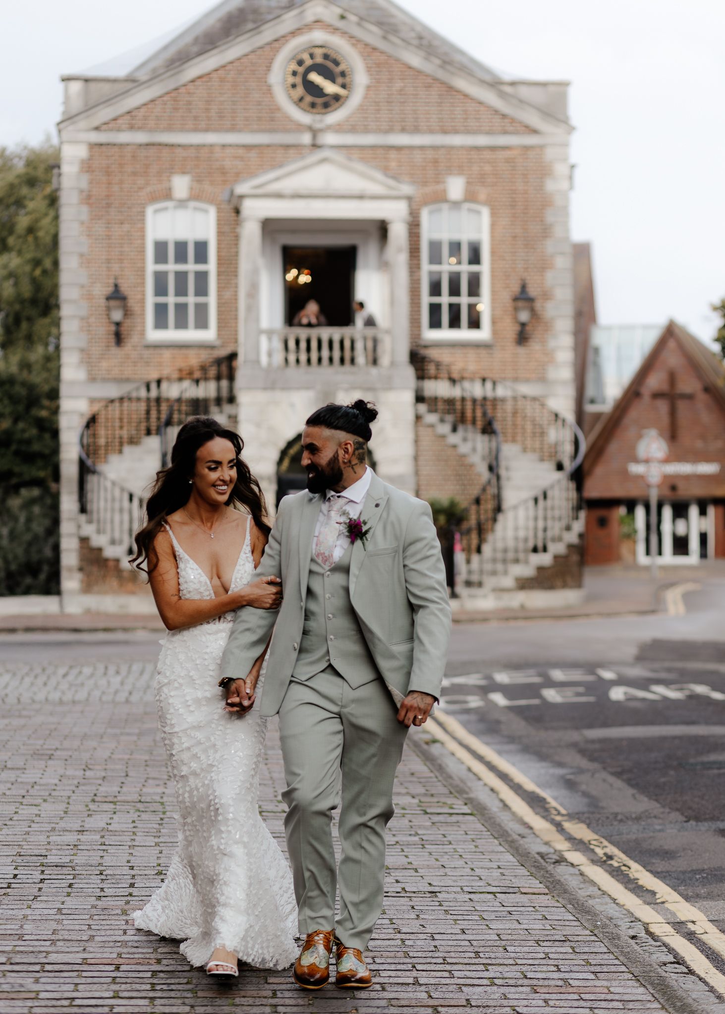 A joyful couple in wedding attire shares a candid moment while walking on a cobblestone street.