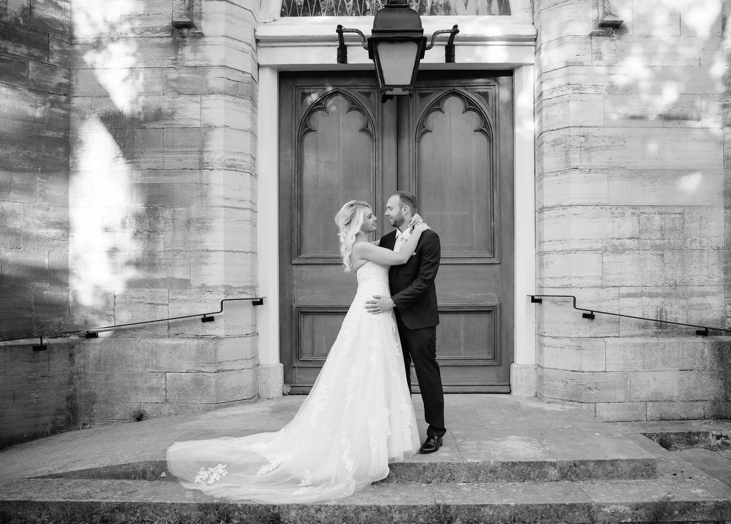Black and white photo of a bride and groom sharing a romantic moment on church steps in wedding attire.