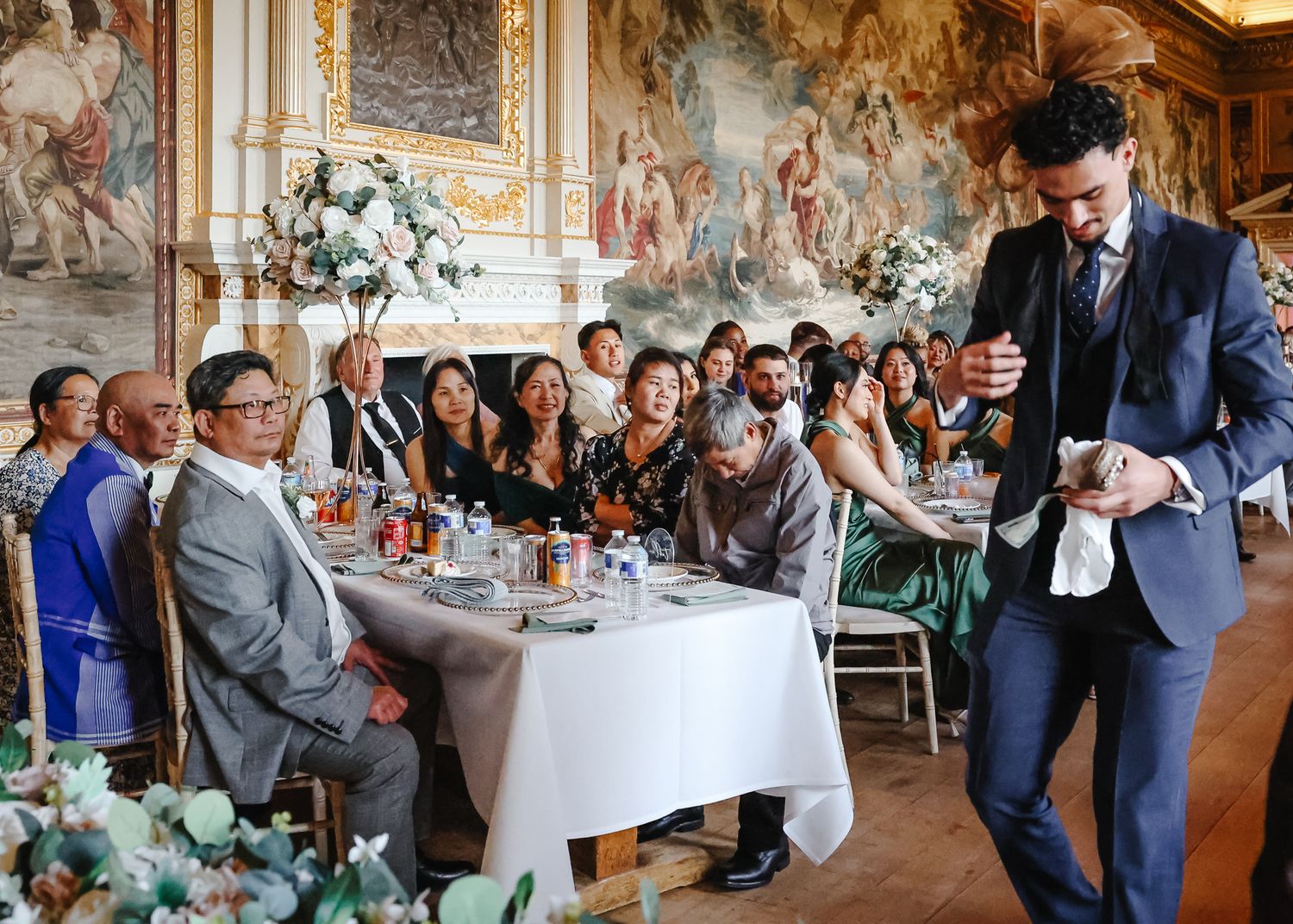 Elegant wedding reception setup in a grand hall with ornate walls and floral centerpieces on dining tables.