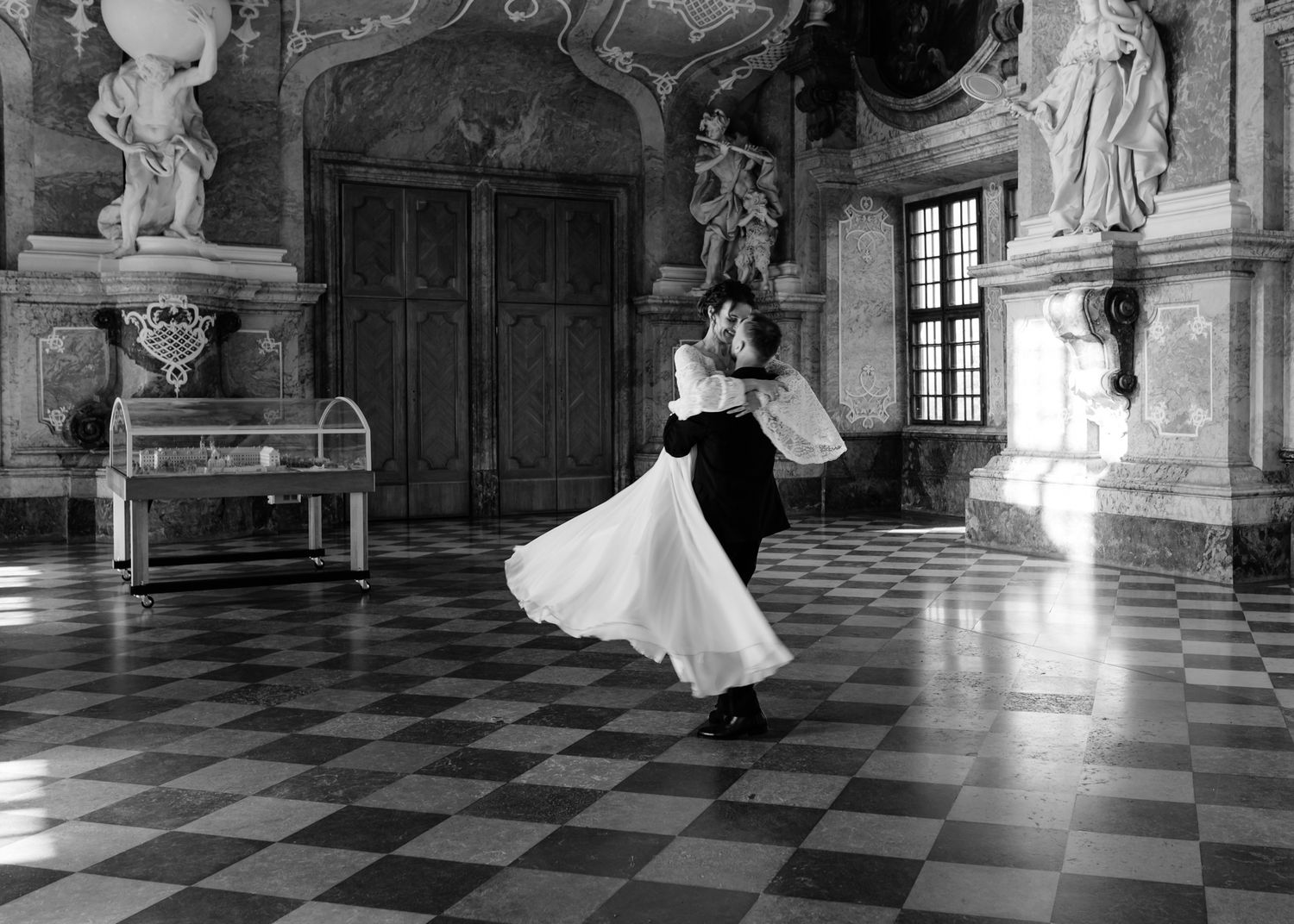 Black and white panoramic view of a luxurious baroque palace interior with marble floors and statuary.