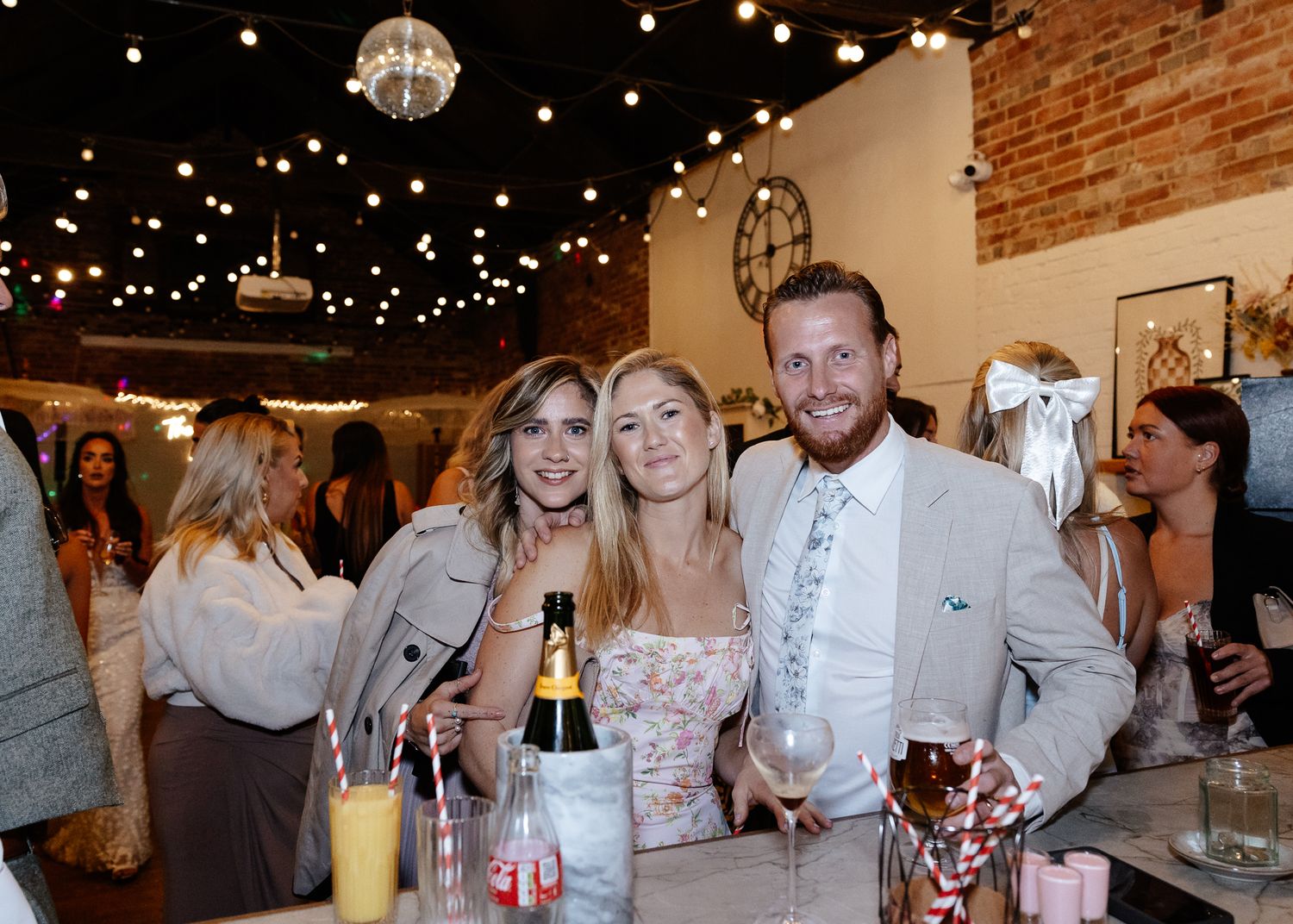 People celebrating at a rustic indoor venue with exposed brick walls and twinkling lights overhead.