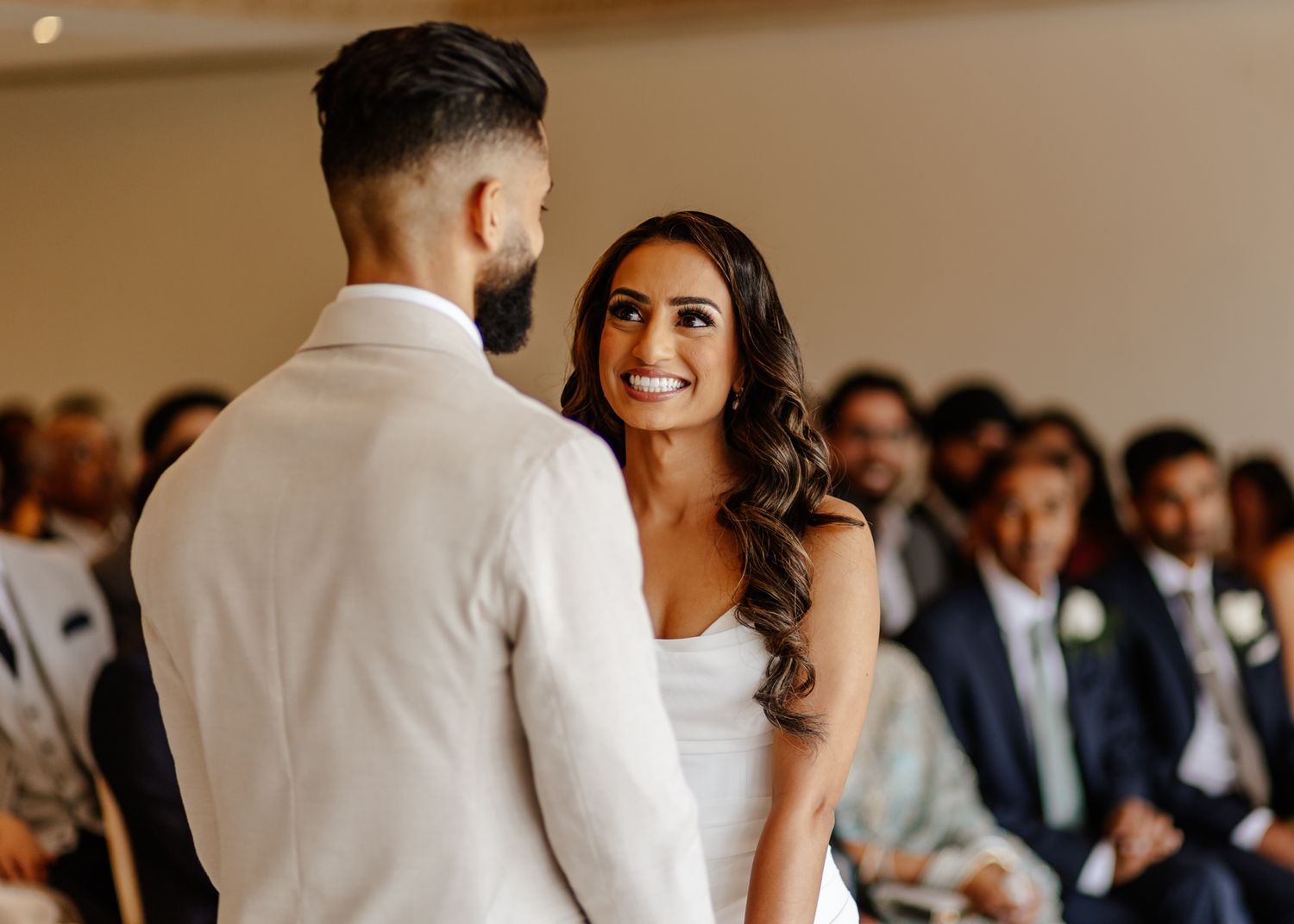 A wedding reception scene with guests gathered around tables in a bright, elegant venue.