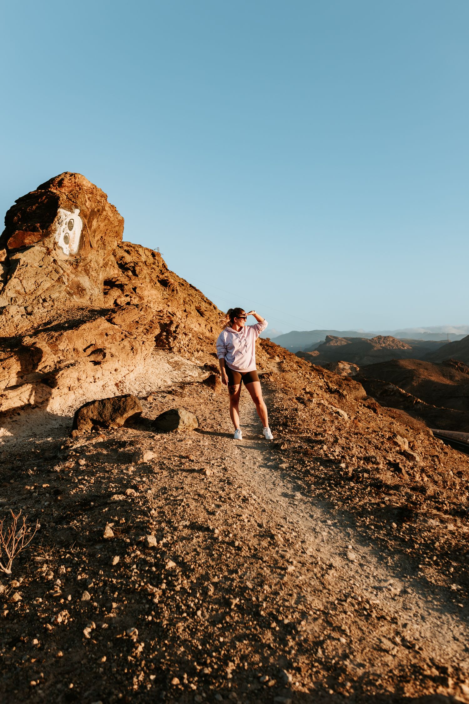 A couple embraces on a rocky mountain peak during golden hour with scenic mountain views in the background.