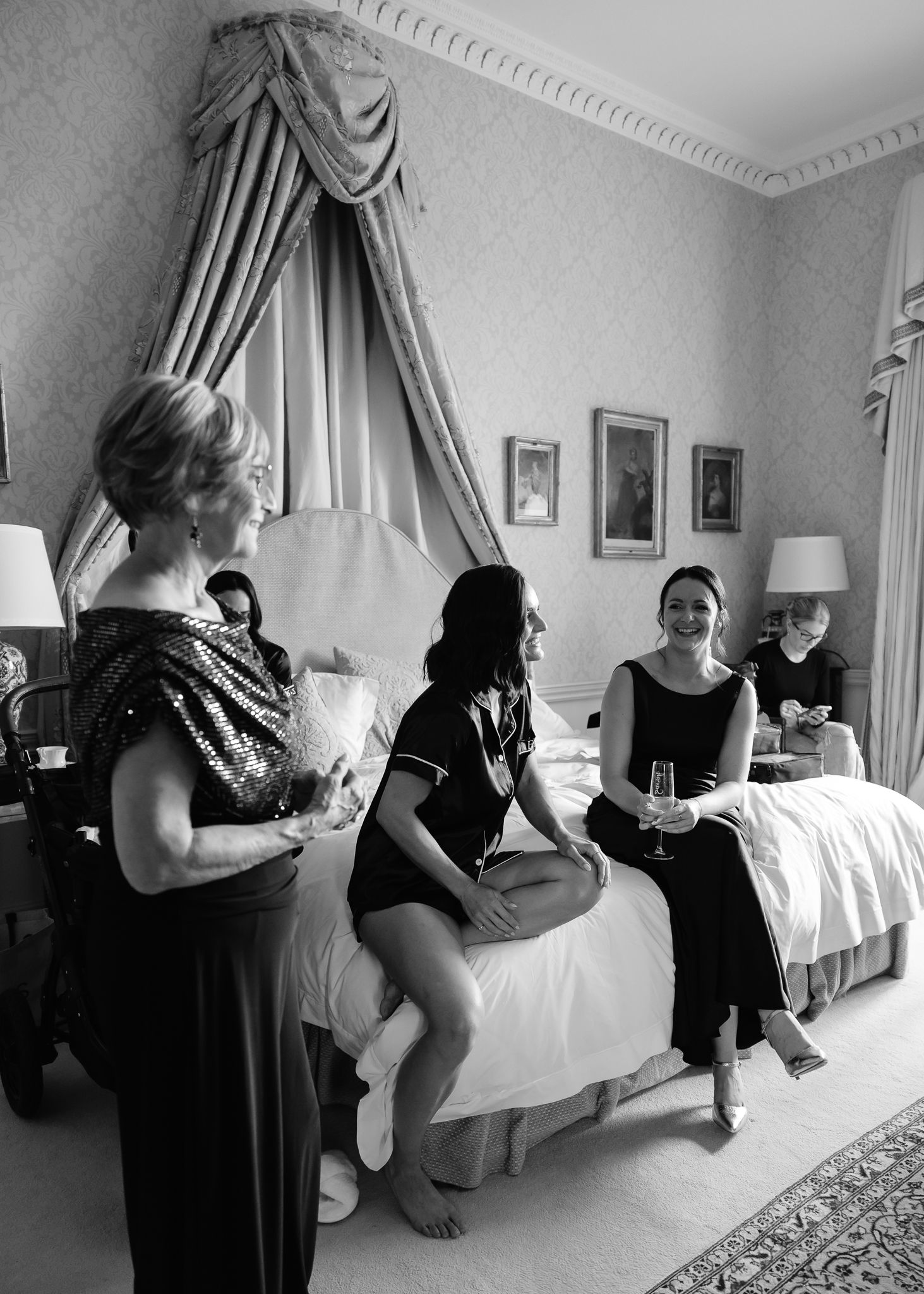 Group gathered in elegant hotel room with white bedding and curtains during preparation event.