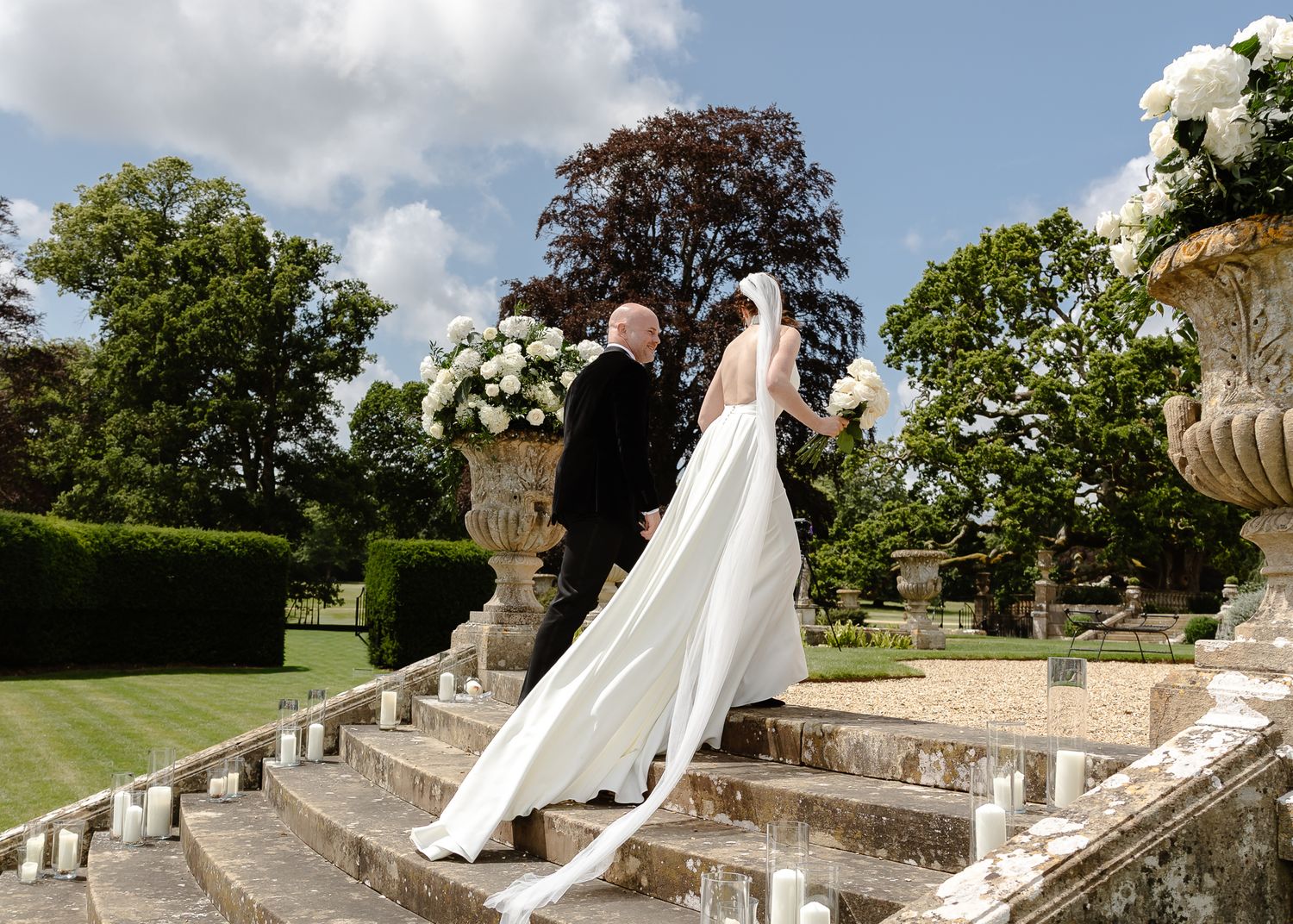 Wedding couple poses on grand stone staircase with ornate architectural details.