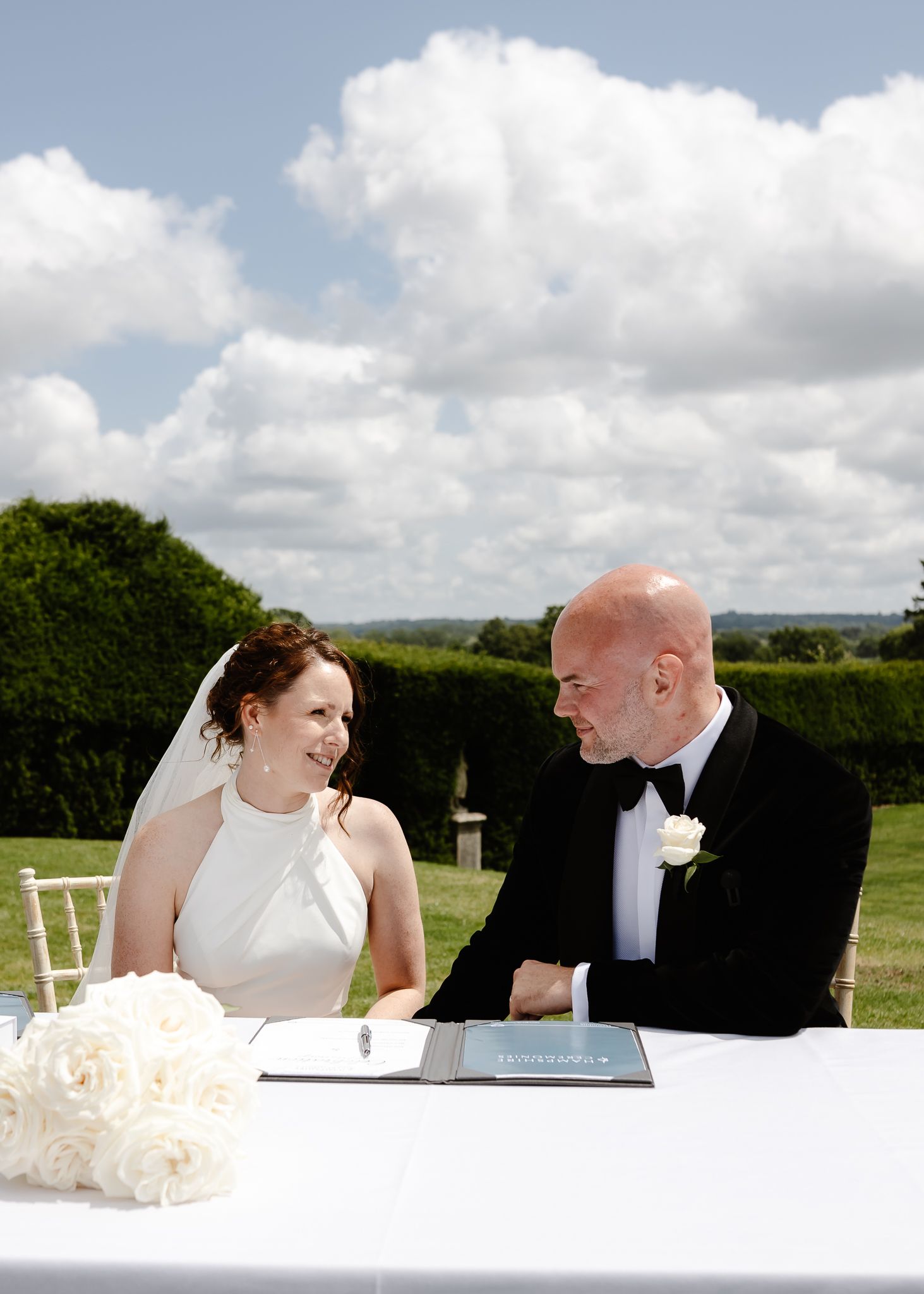 Elegant wedding table setting in an outdoor venue with white chairs and floral arrangements.